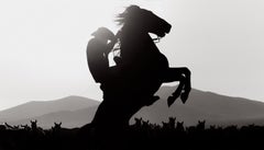 Cowboy in sella al suo cavallo che si staglia contro la mandria e le montagne