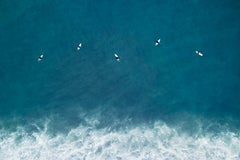Cinq surfeurs attendent le prochain ensemble de vagues au milieu de la mer céruléenne