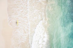 Lone surfer with a yellow board walks across the shore seeking the perfect wave