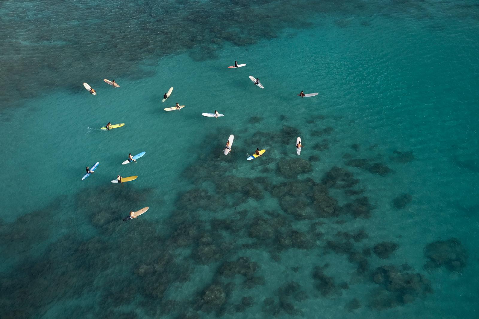 I longboarder aspettano le onde sulle loro tavole colorate in questa foto aerea - Photograph di Drew Doggett