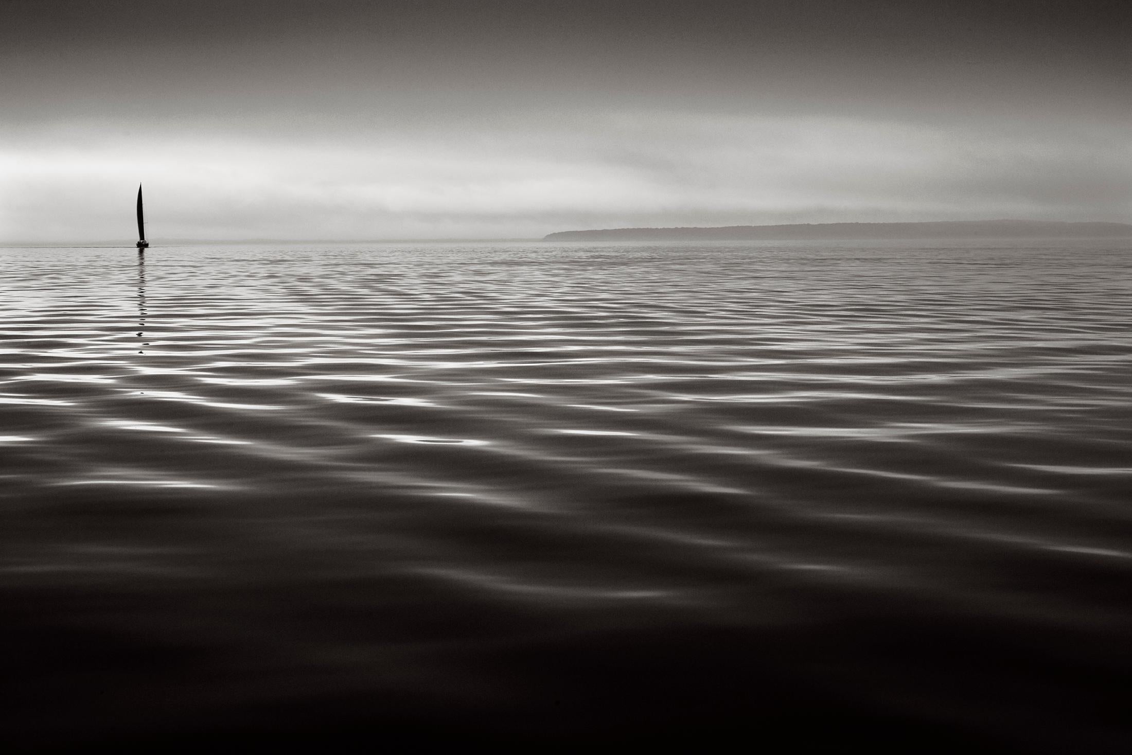 Una meditativa fotografia in bianco e nero con uno yacht solitario su acque calme - Photograph di Drew Doggett