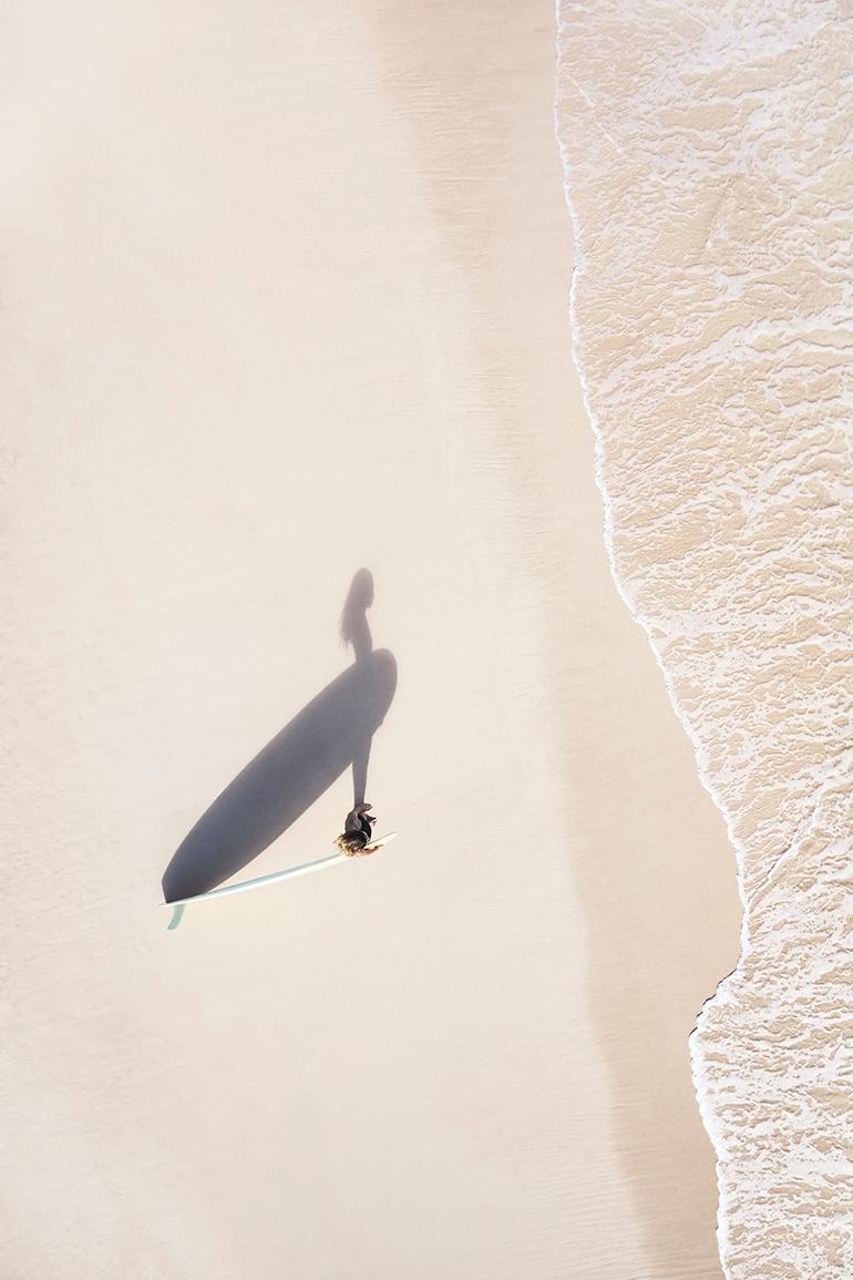 "Call of the Sea" 

In this calming, best-selling image, a lone surfer looks over the gentle tide on the velvet sand of Oahu. 

The print series Swell: Endless Blue takes you on a sweeping yet intimate aerial journey above some of the most