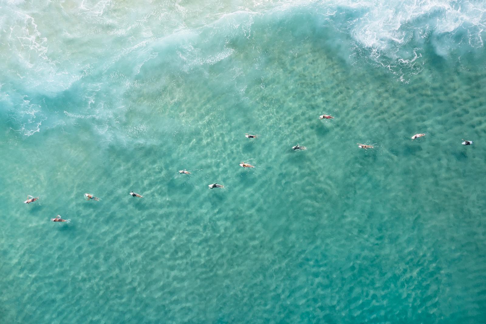 I surfisti si mettono in fila per una serie di onde sul mare blu in questa foto a colori - Photograph di Drew Doggett