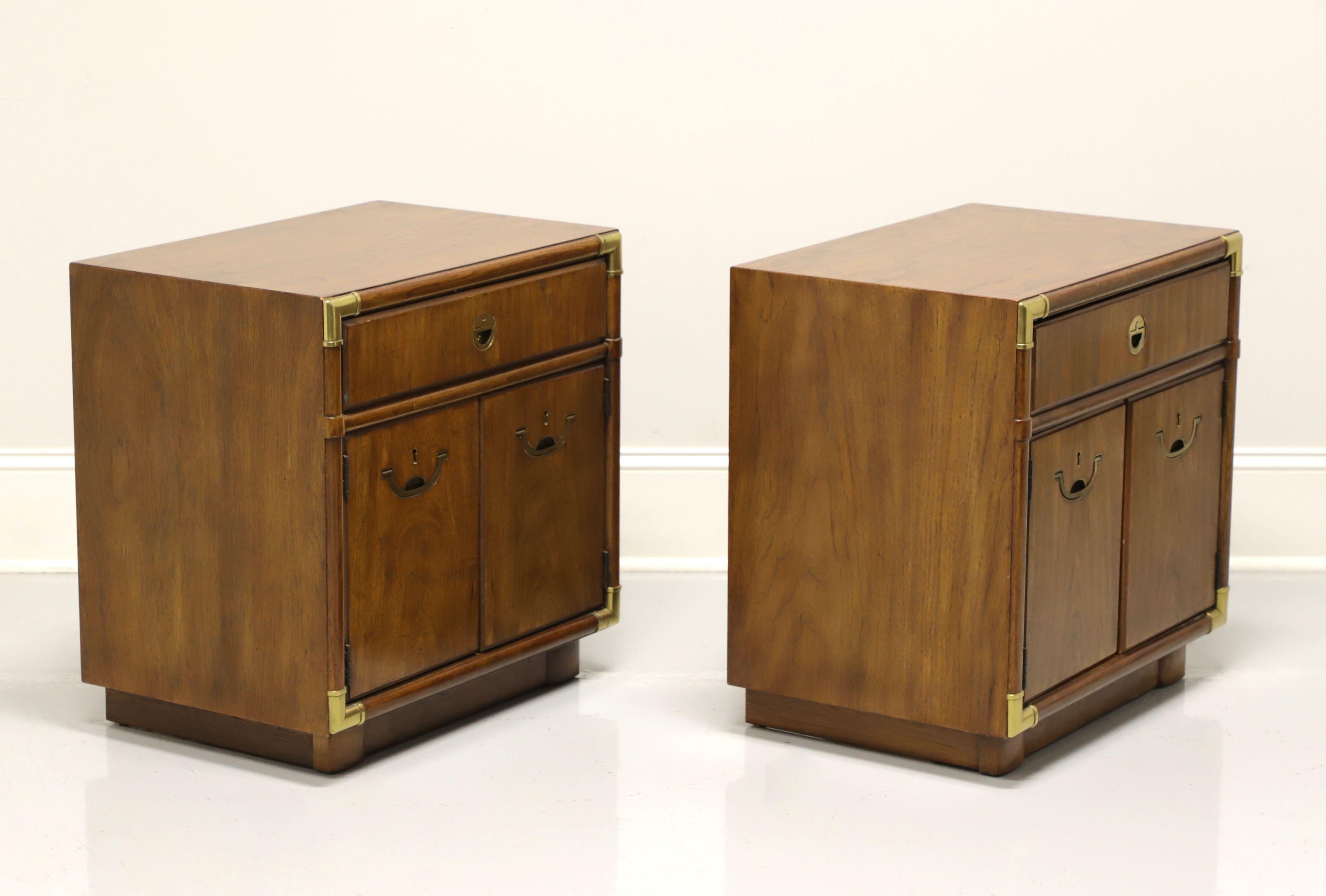 A pair of Campaign style nightstands by Drexel Heritage, from their Accolade Collection. Pecan with brass hardware and decorative accents. Features one drawer of dovetail construction over a two door cabinet with faux lockplates revealing a storage