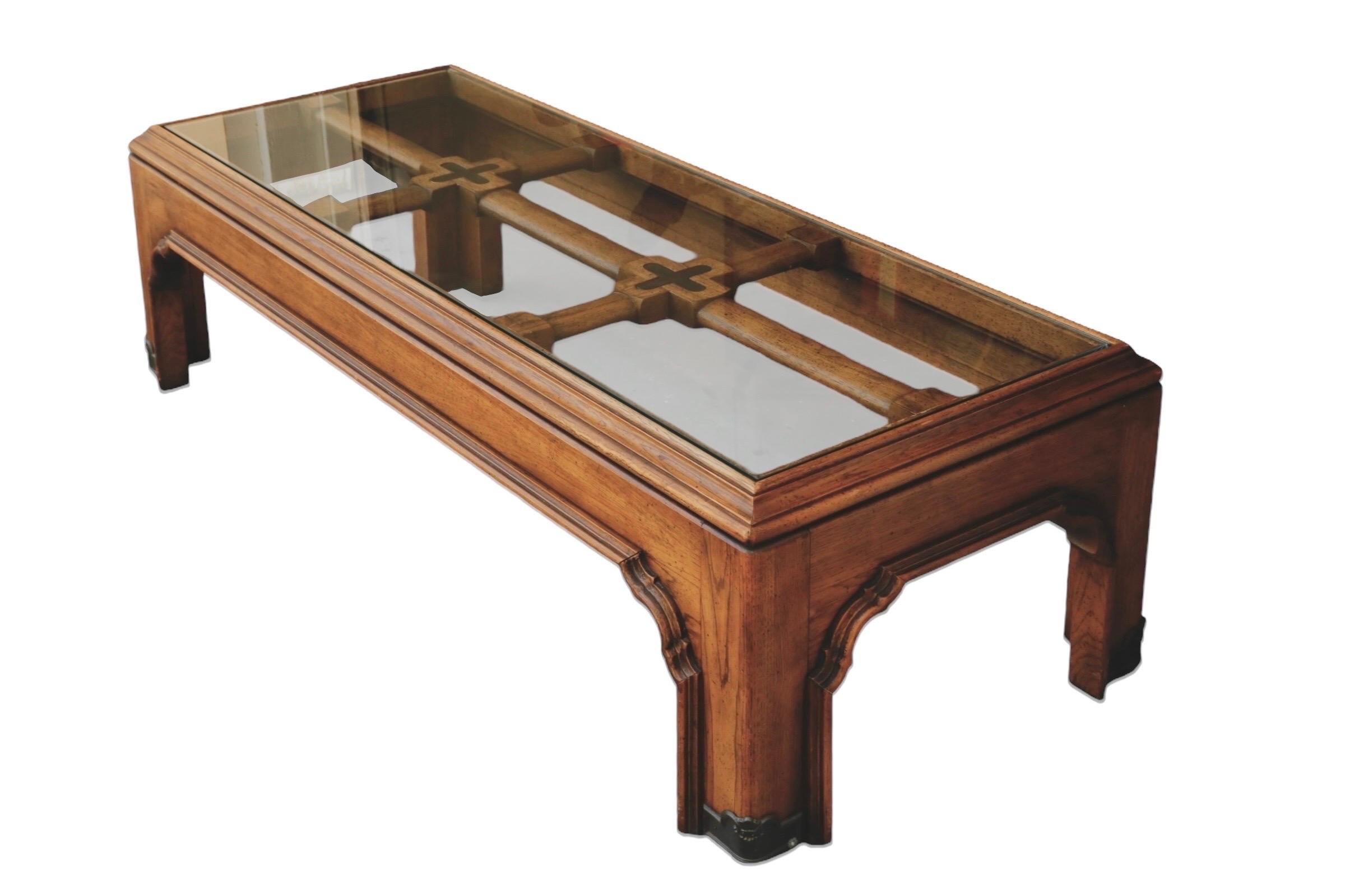 A glass top coffee table attributed to Drexel. The rectangular glass top is supported with a double stretcher inset with gold metal ‘x’s at the joins. The tabletop is framed with an angled beveled edge and the skirt and legs are finished with a