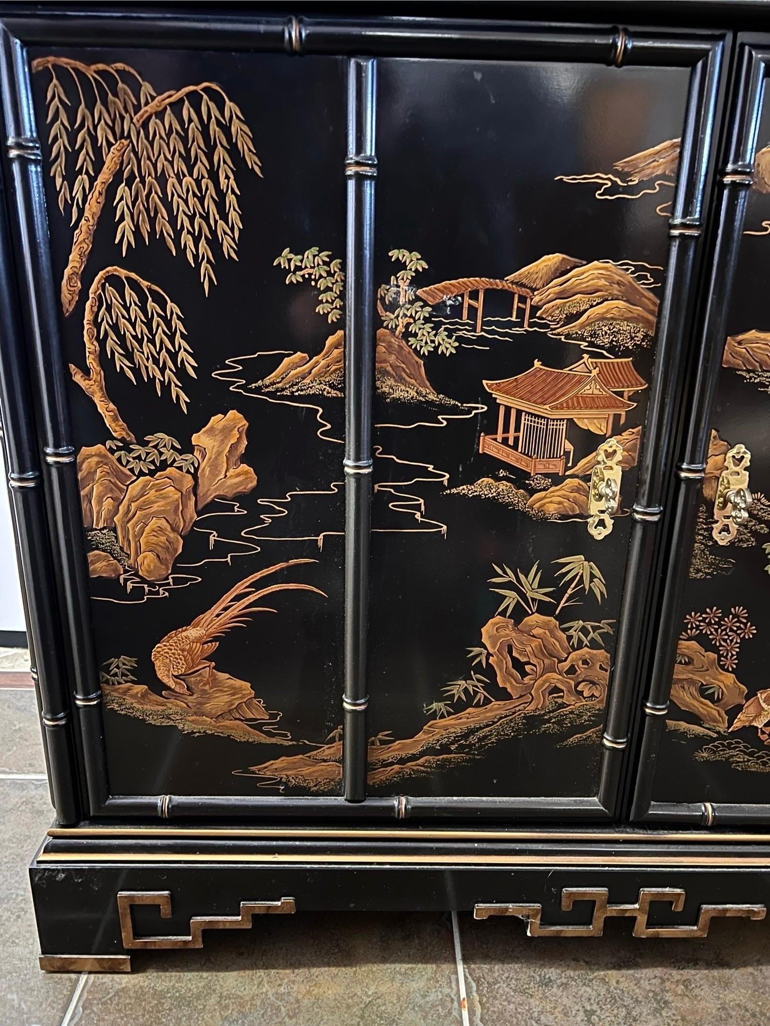 Stunning and breathtaking black lacquered chinoiserie style armoire that features a gold pagoda with faux bamboo accent detail all around.  It alos features hand painted landscape scenery by skilled artisans throughout.
The top portion has two