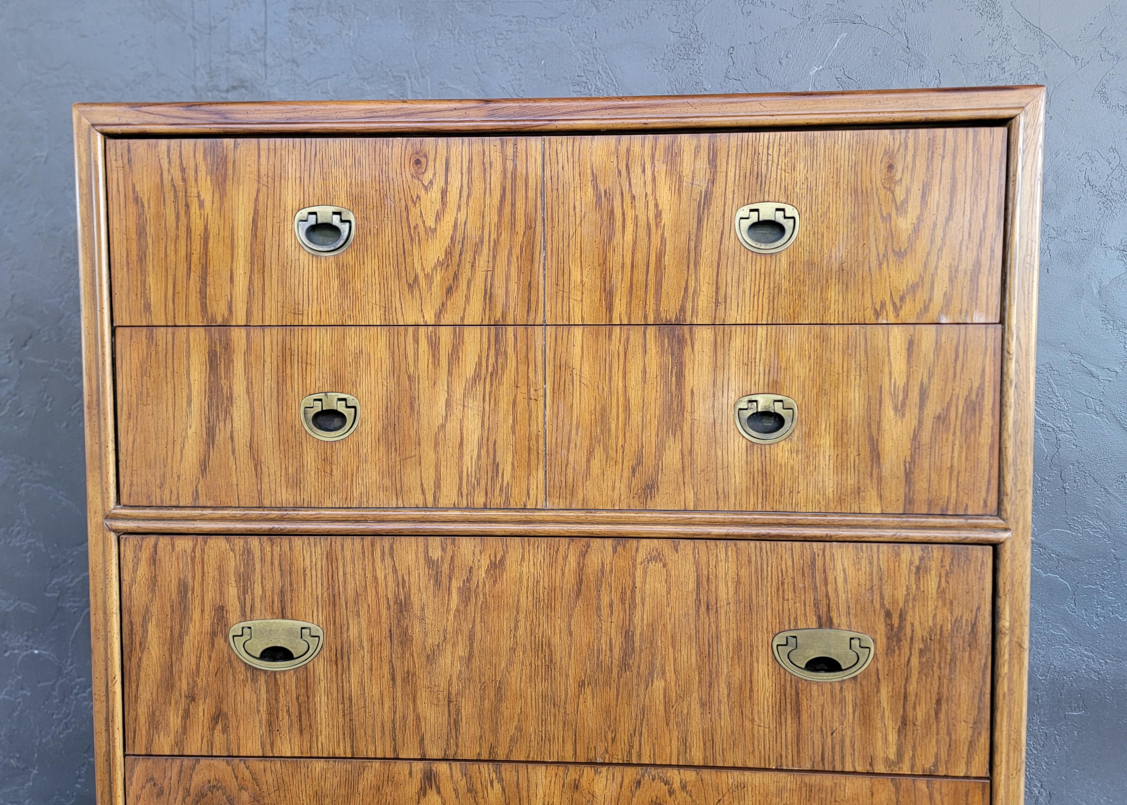 A Drexel Campaign style highboy chest of drawers. Circa. 1970's. Quality materials and craftsmanship with solid oak interior wood and dovetail construction. Inset brass pulls. Drawers glide easily as intended, interior of drawers are very nice.