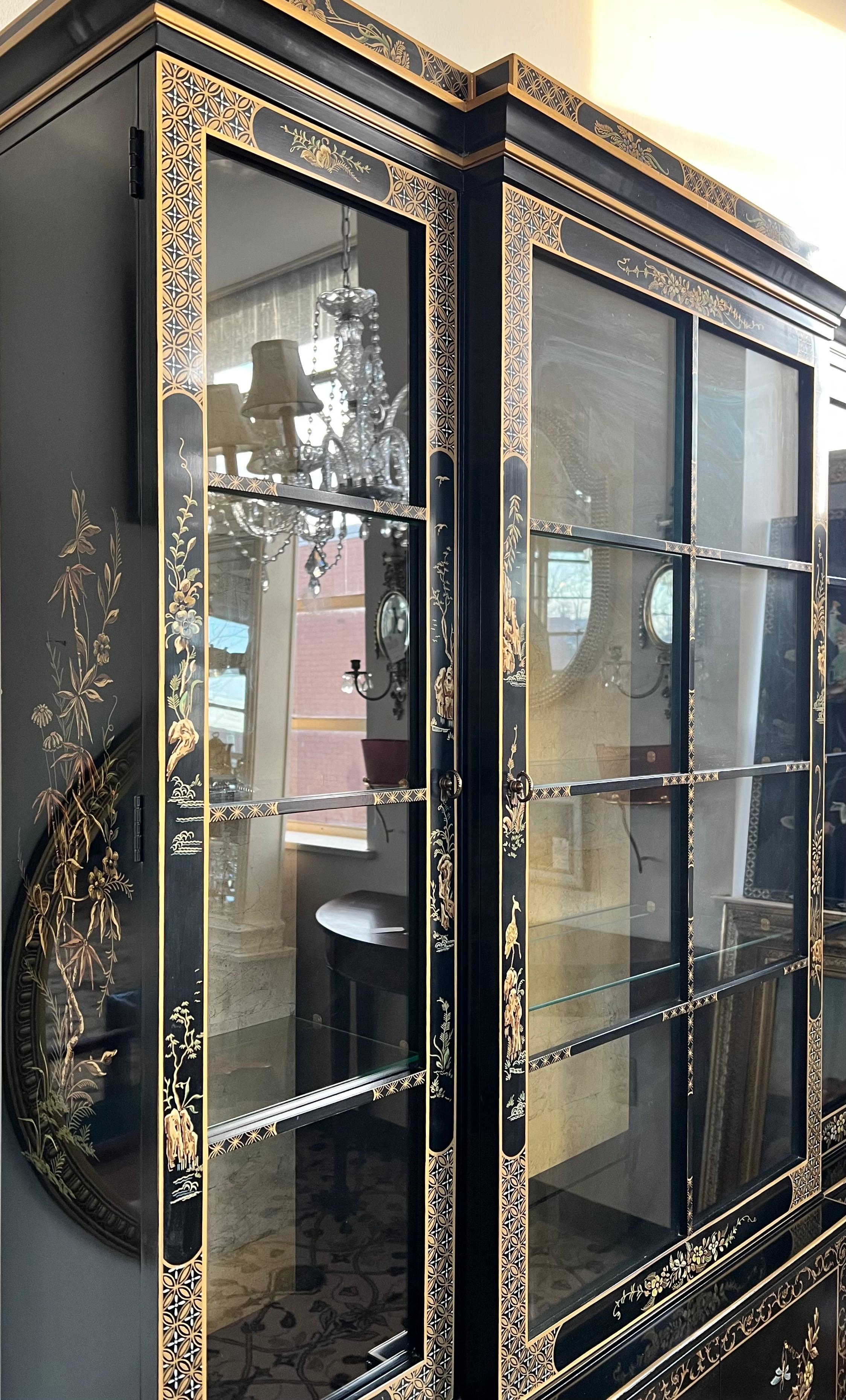 Beautiful black laquered china display cabinet in excellent condition. It features chinoiserie handpainted gold scenery and glass on three sides. The doors open to glass shelves which are illuminated from above and has a gold leaf background. Bottom