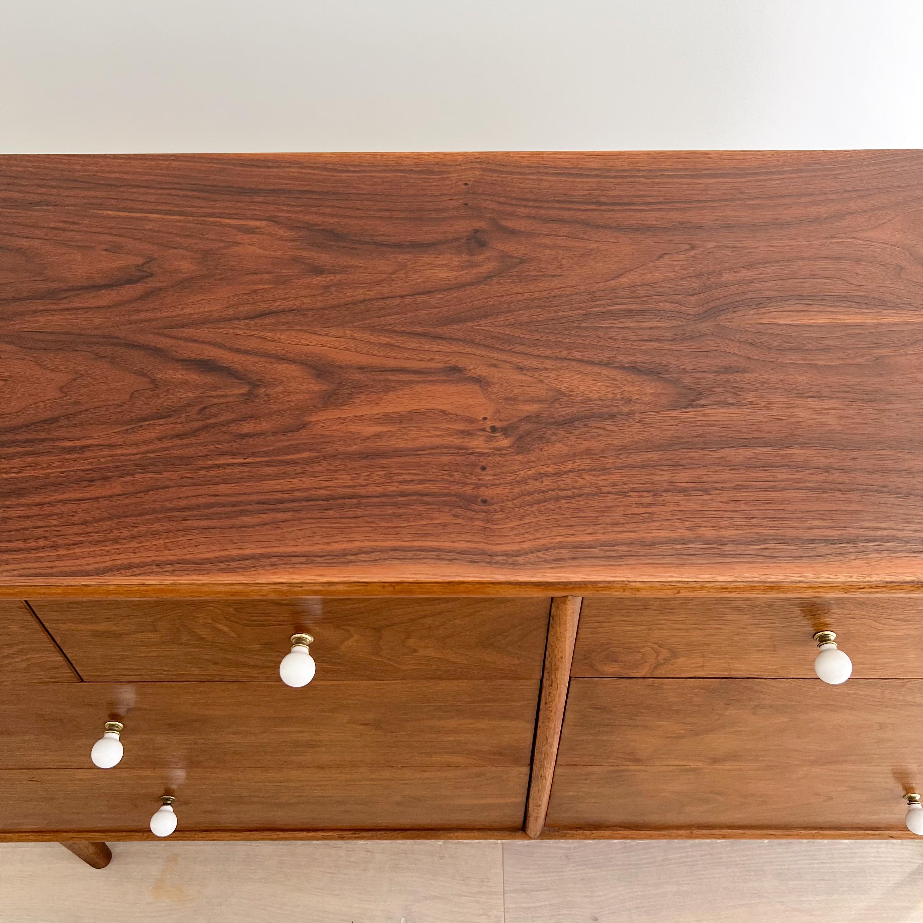 Mid Century Drexel declaration low dresser by Kipp Stewart & Stewart McDougall. This piece features bookmatched black walnut grains and includes their signature porcelain knobs. Includes plenty of storage with eight dovetailed drawers.