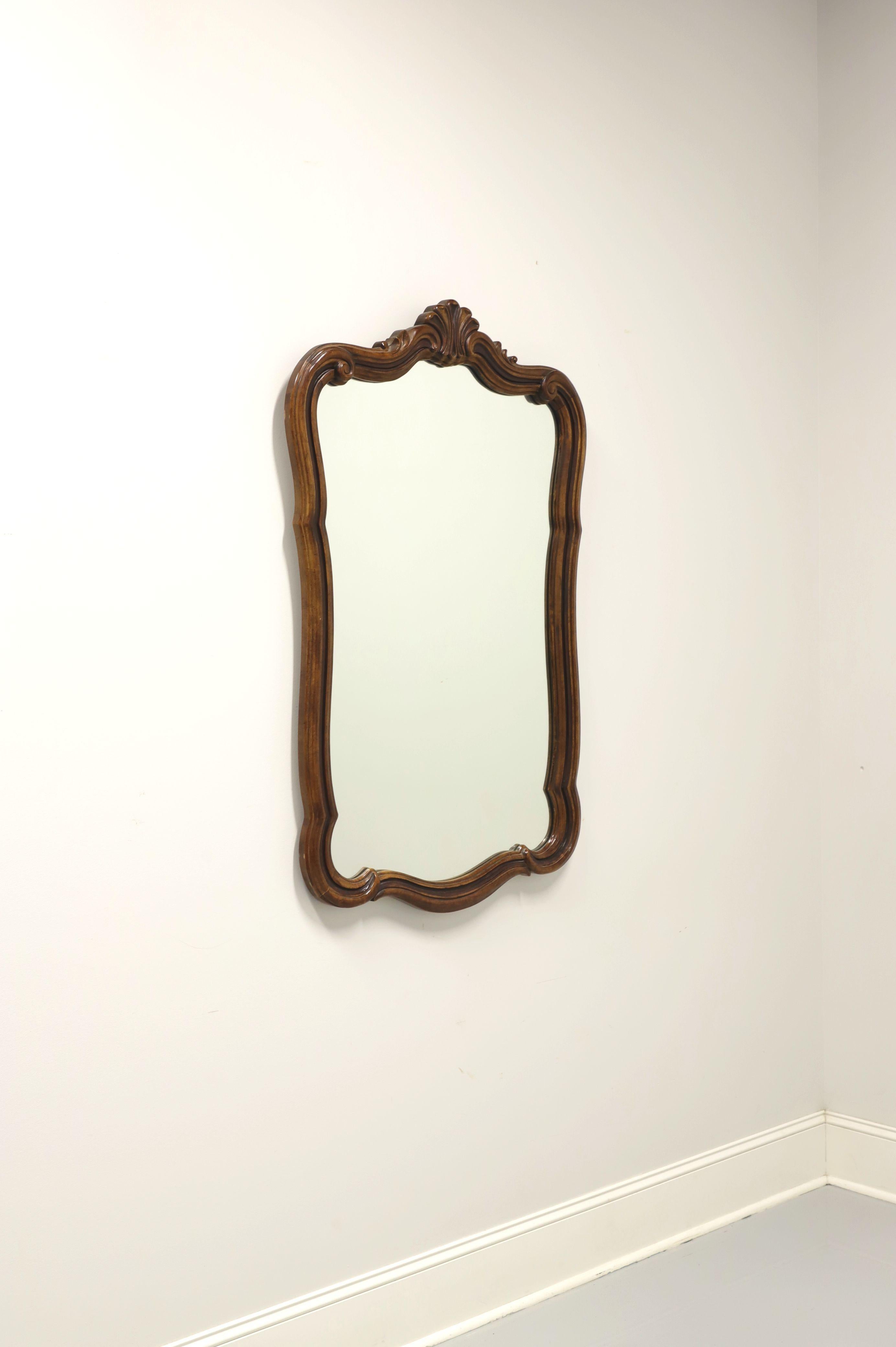 A French Country style wall mirror by Drexel Heritage, from their Grand Tour Collection. Mirror glass and slightly distressed walnut frame with decorative scroll design and carved fan to top. Made in North Carolina, USA, circa 1977. 

Style #: