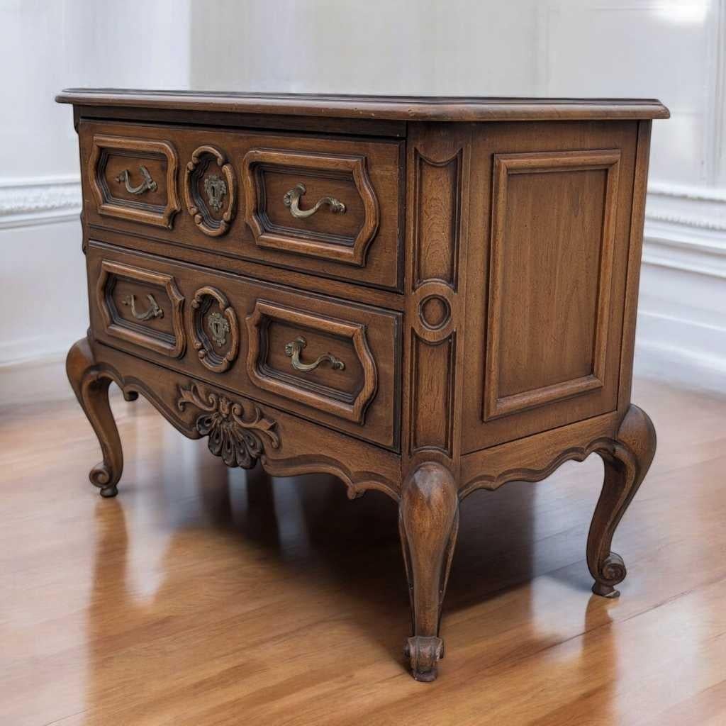 Charmante commode de style provincial français de Drexel, fabriquée au milieu du 20e siècle en bois massif et présentant des façades de tiroirs sculptées, des pieds en cabriole et des ferrures en laiton d'origine. Cette élégante pièce à deux tiroirs
