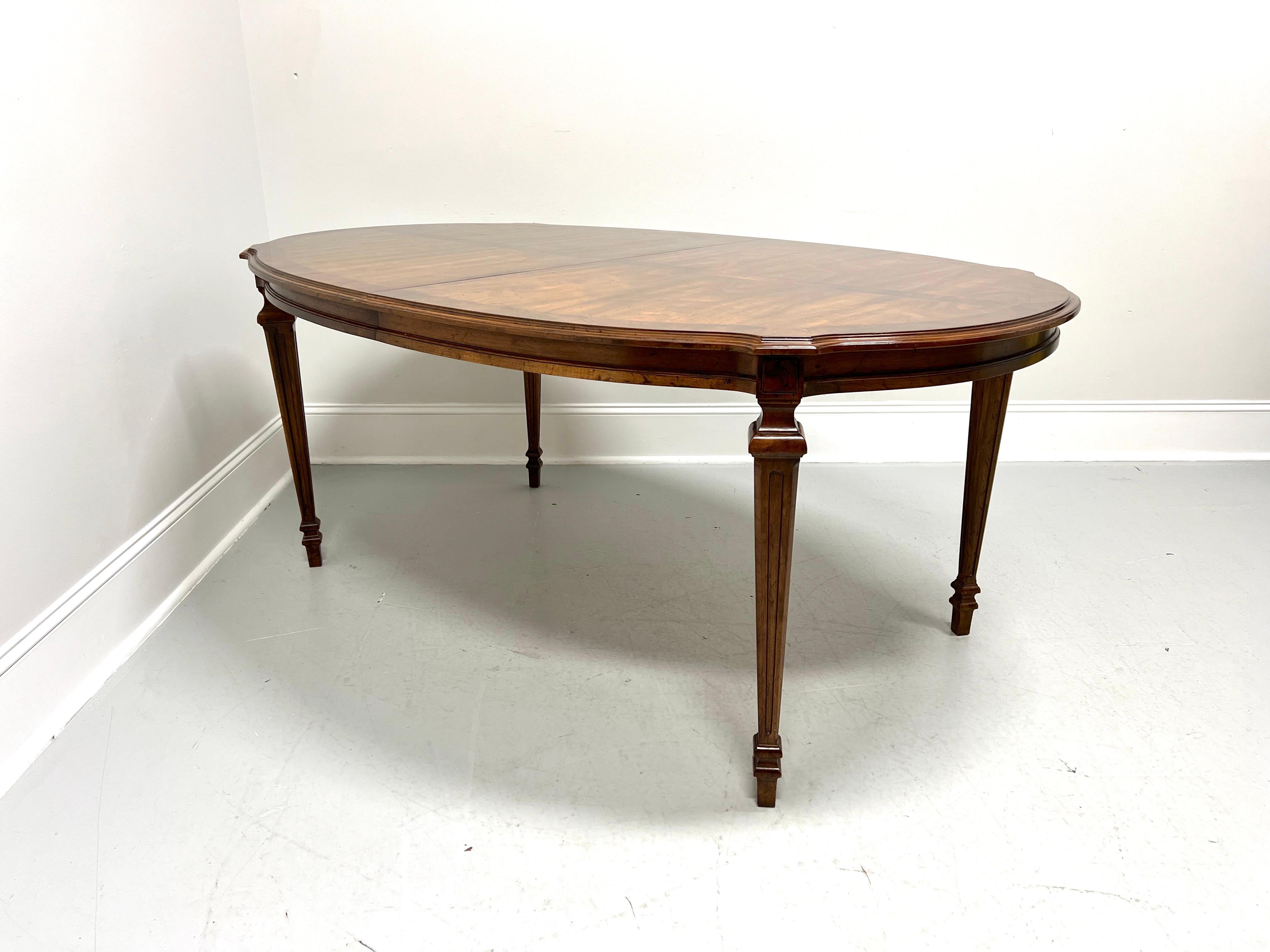 An oval dining table in the French Provincial Louis XVI style by Drexel Heritage. Walnut & burl walnut with inlaid & banded top, serpentine ogee edge to top, carved apron, fluted tapered straight legs, and spade feet. Includes two 22 inch extension