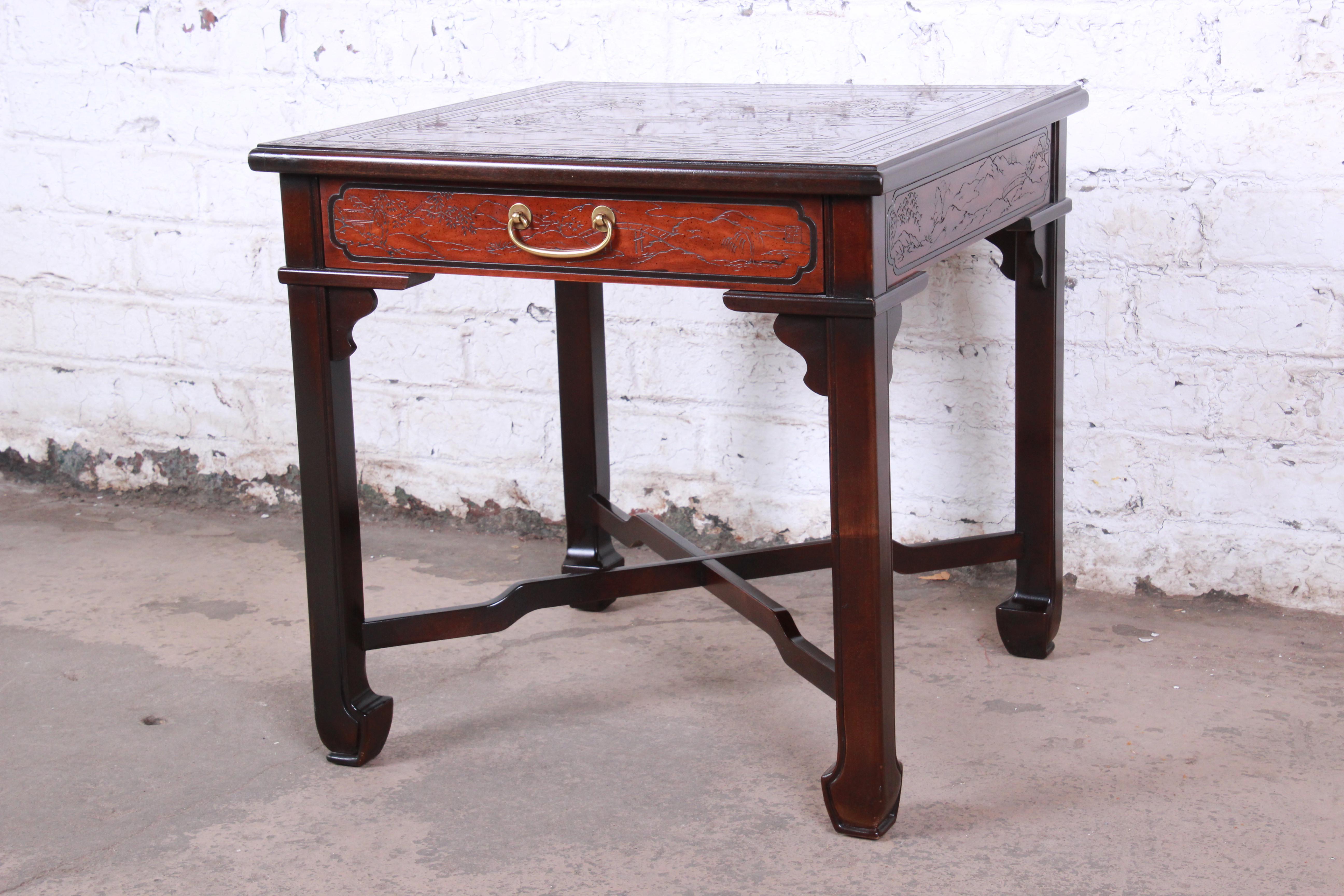 A gorgeous Hollywood Regency Chinoiserie x-base side table from the Connoisseur line by Drexel Heritage. The table features beautiful mahogany wood grain and nice carved Asian details with nature scenes. It has a single drawer with the original