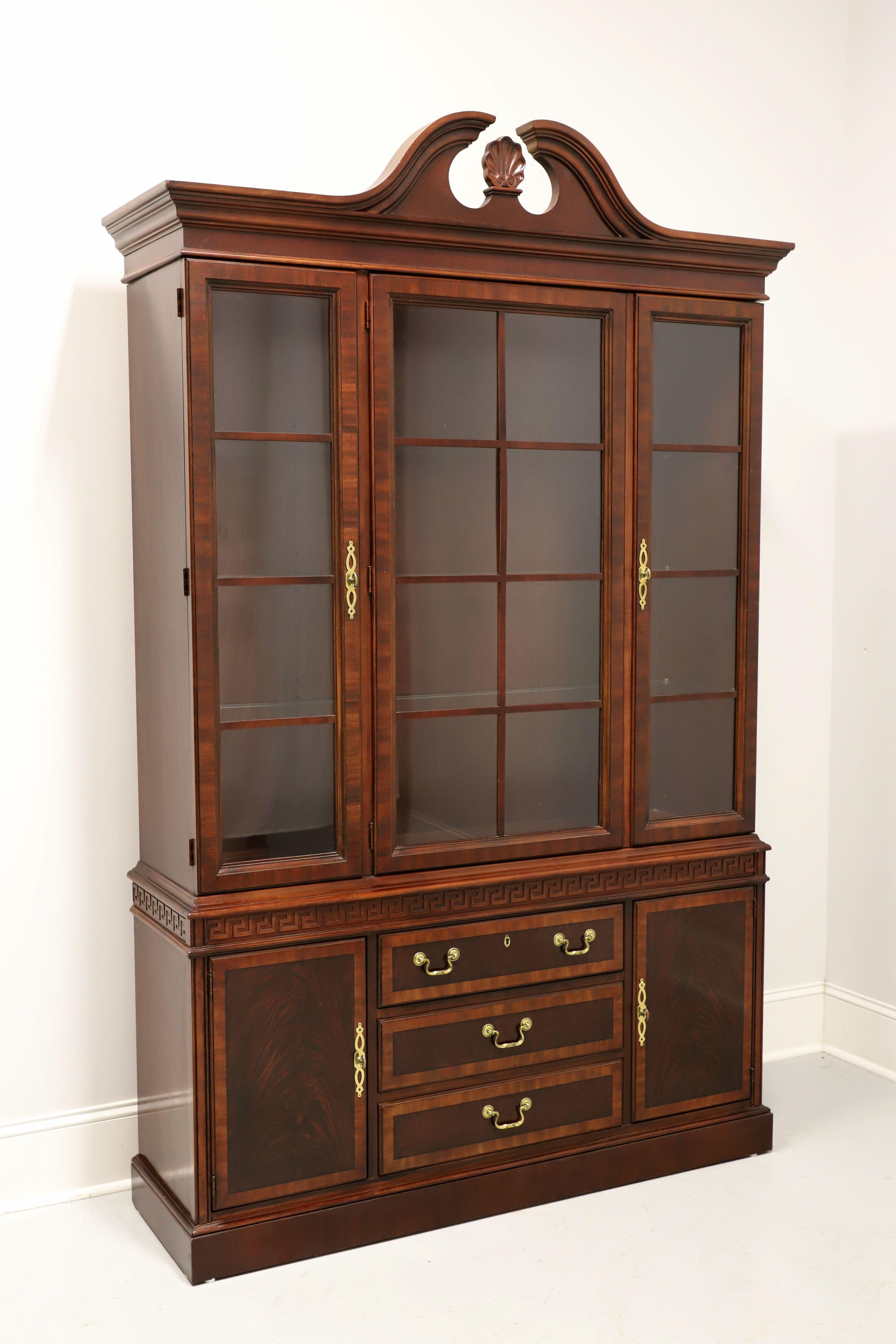 A Chippendale style china cabinet by Drexel Heritage. Mahogany with inlaid flame mahogany, brass hardware, crown moulding with pediment to top, banded door & drawer fronts, decoratively carved frieze to center, and a solid base. Upper lighted