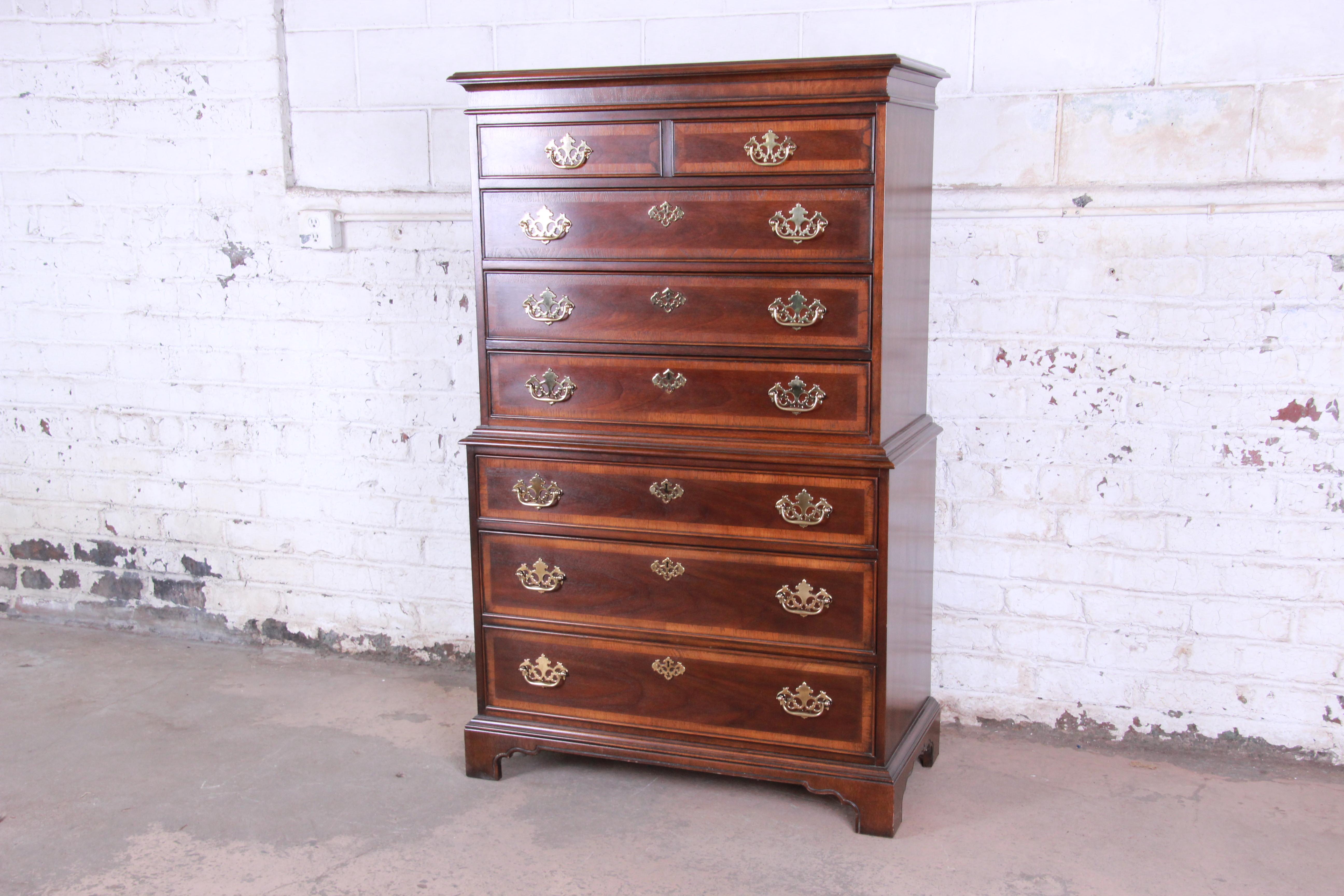 A beautiful Chippendale style banded mahogany highboy dresser by Drexel Heritage. The dresser features a traditional English style, gorgeous mahogany wood grain with a nice banded edge, and original brass hardware. It offers ample room for storage,