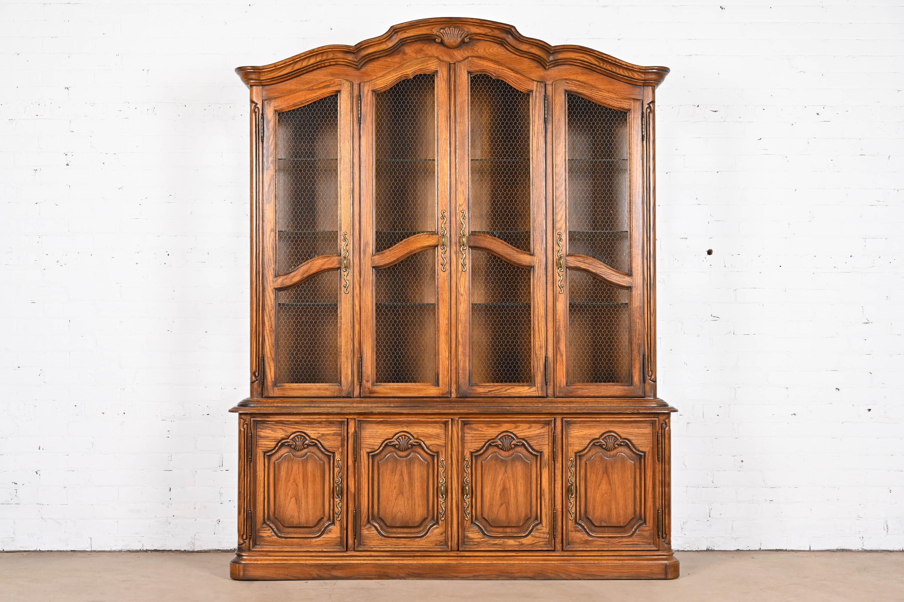 A beautiful French Provincial Louis XV style lighted breakfront bookcase or dining cabinet

By Drexel Heritage

USA, 1970s

Carved oak, with glass shelves and original brass hardware.

Measures: 66