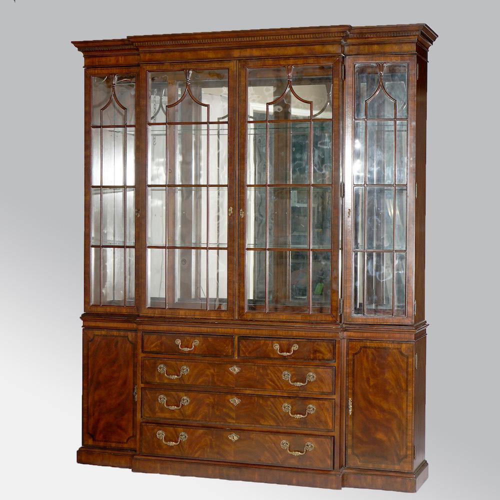 A Georgian style breakfront buffet cabinet by Drexel Heritage offers flame mahogany construction with upper having glass doors opening to lighted, shelved and mirrored display interior over lower case with drawer column with flanking cabinets, maker