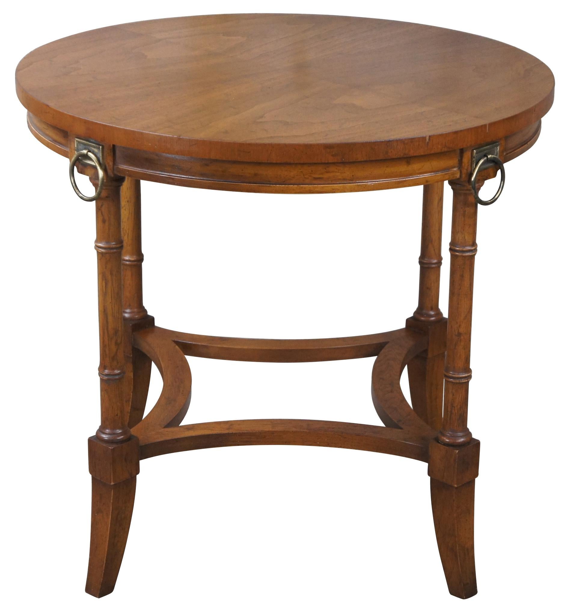 Mid century Drexel Heritage grand tour accent table. Drawing inspiration from French Empire and British Campaign styling. A round form made from walnut with a matchbook top, brass ring knocker accents and faux bamboo columns. Circa 1965, 23-546-41,