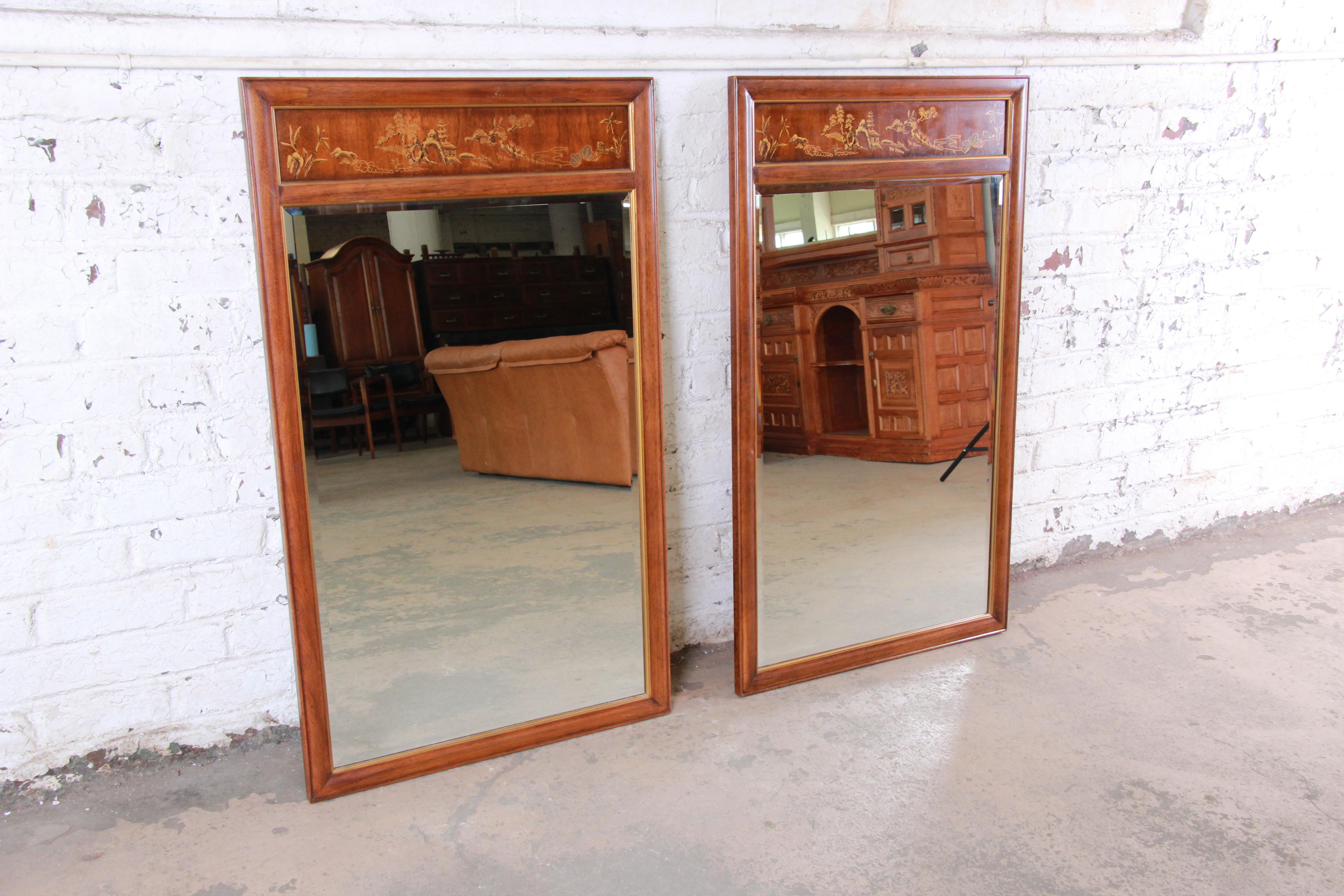 An gorgeous pair of Hollywood Regency chinoiserie beveled wall mirrors from the Dynasty Collection by Drexel Heritage. The mirrors feature gorgeous walnut wood grain and beautiful painted Asian nature scenes. The original label is present on the