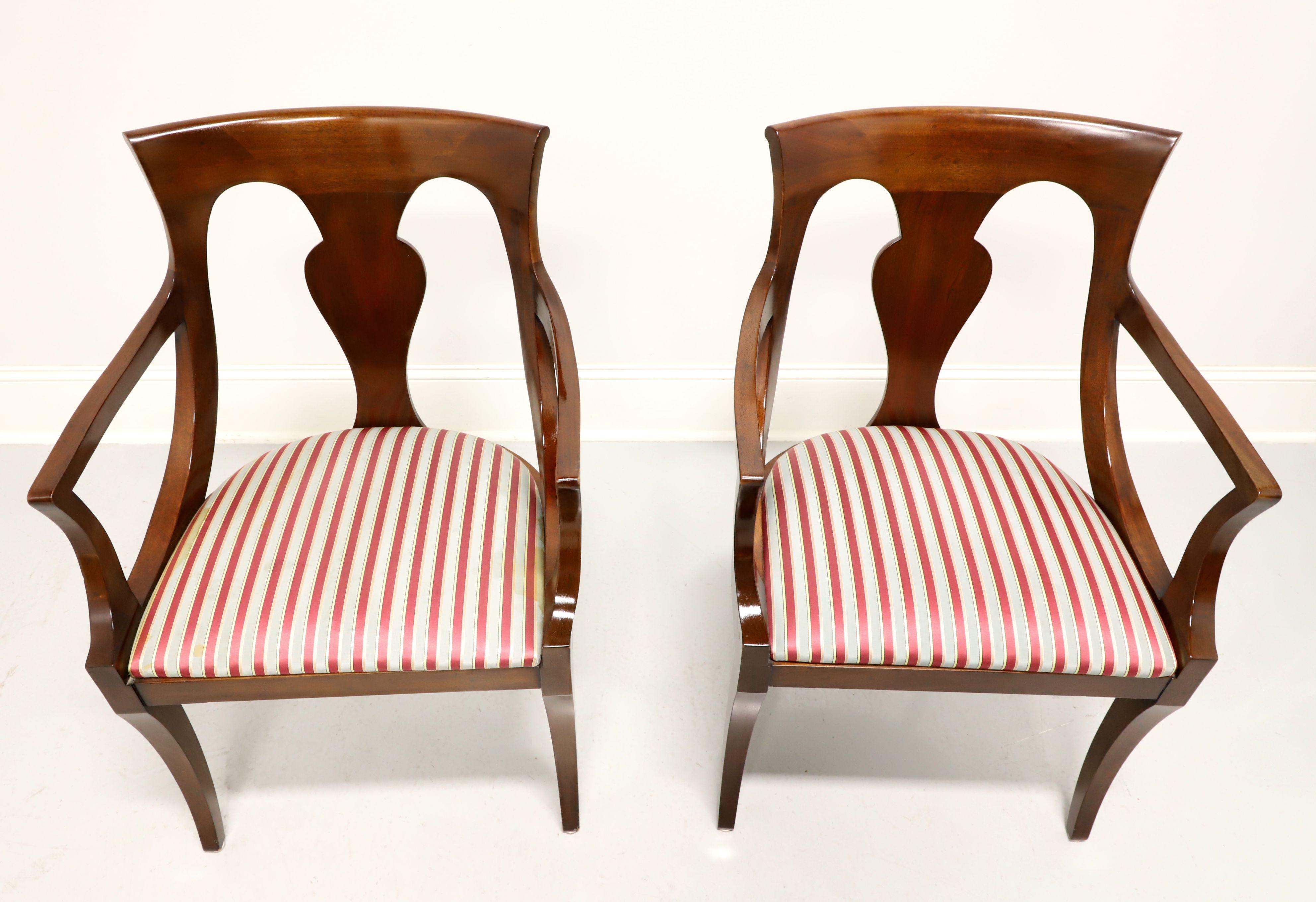 A pair of dining armchairs in the Empire style by Drexel Heritage. Solid mahogany with carved barback crest rail, carved backrest, curved arms, upholstered seat in a red & silver colored stripe fabric and saber legs. Made in Morganton, North
