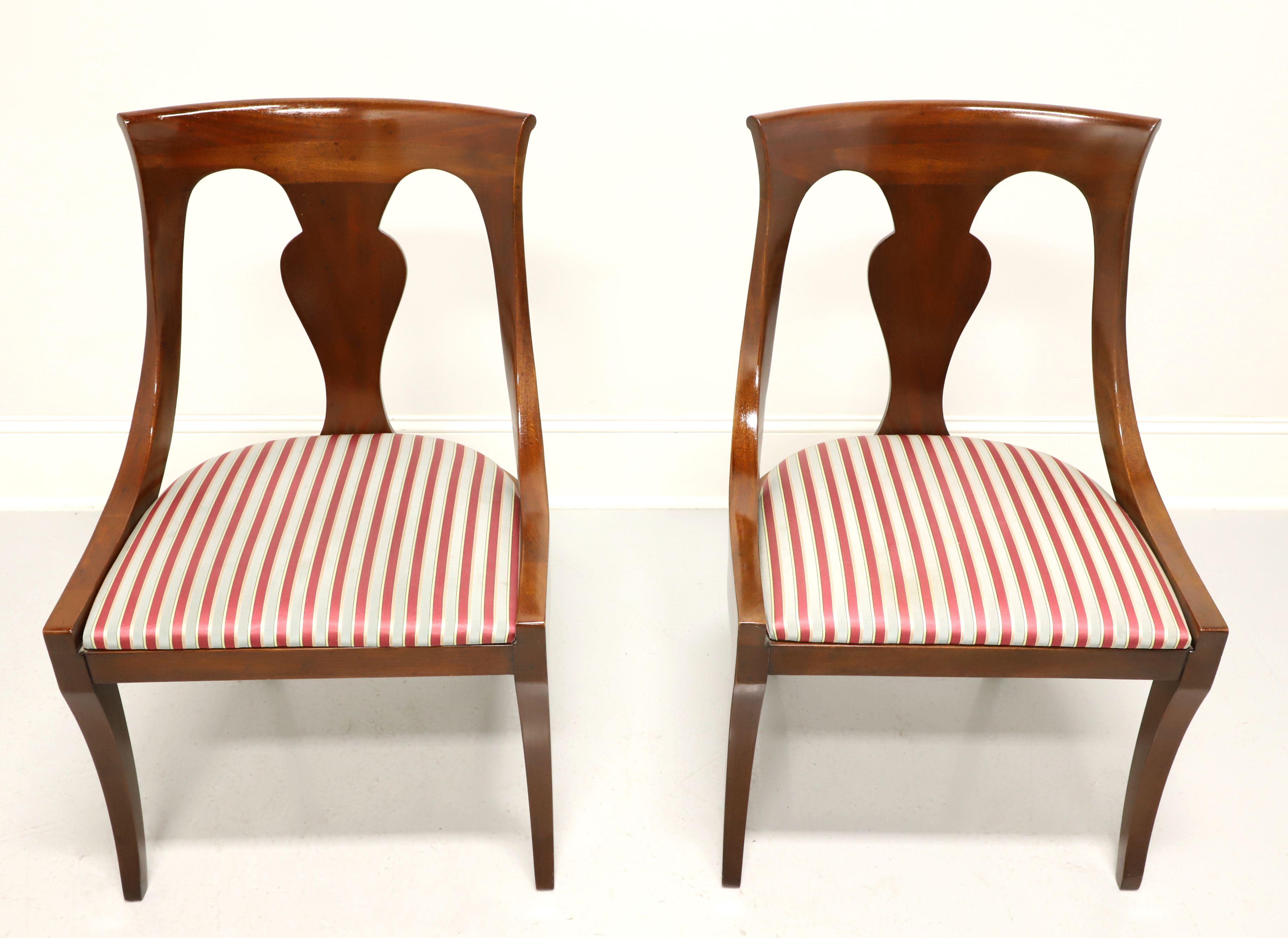A pair of dining side chairs in the Empire style by Drexel Heritage. Solid mahogany with carved barback crest rail, carved backrest, upholstered seat in a red & silver colored stripe fabric and saber legs. Made in Morganton, North Carolina, USA, in