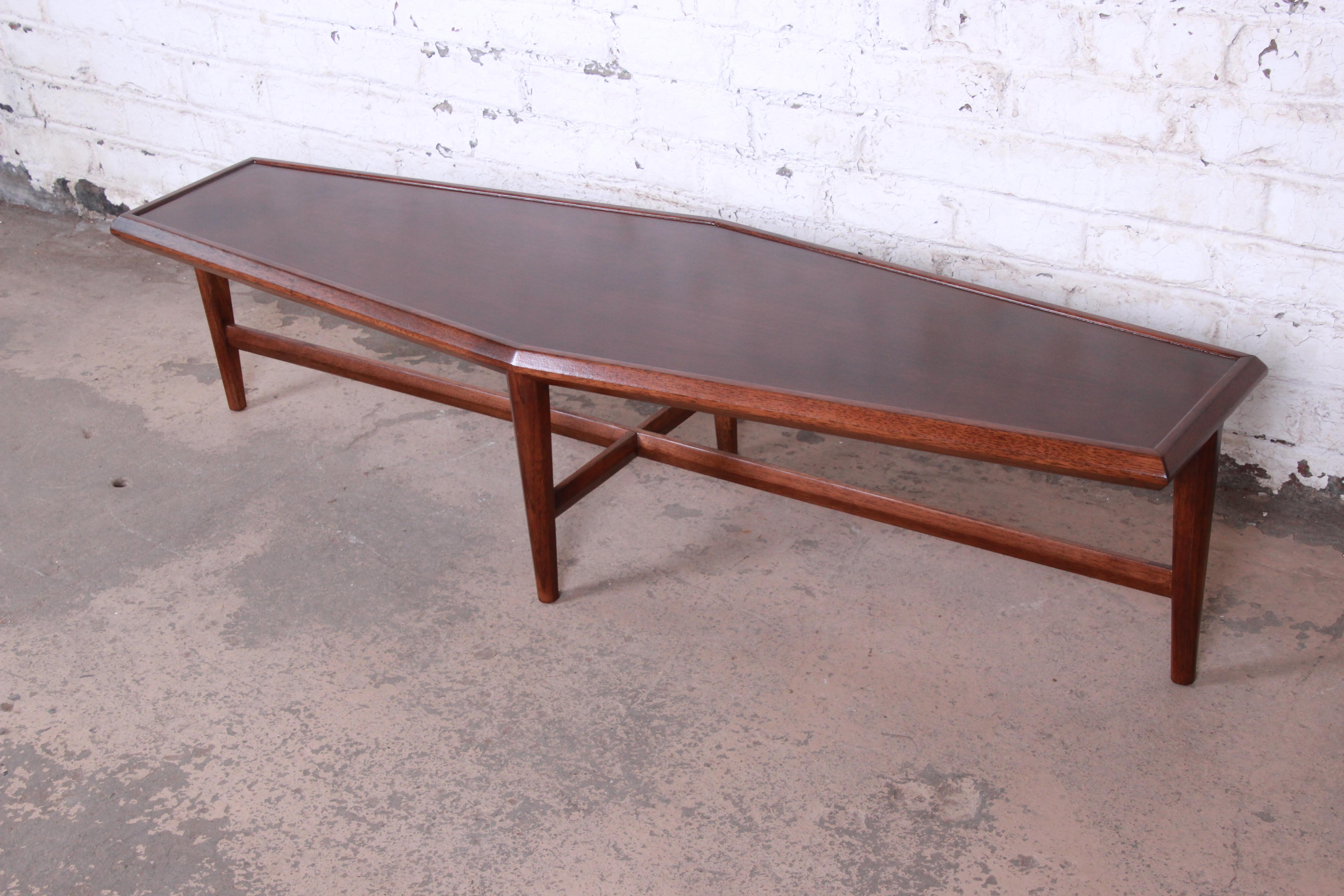 An exceptional Mid-Century Modern boat-shaped coffee or cocktail table by Drexel Heritage. The table features stunning walnut wood grain, with sculpted solid walnut legs and stretchers. It has a unique boat-shaped top. The original label is present