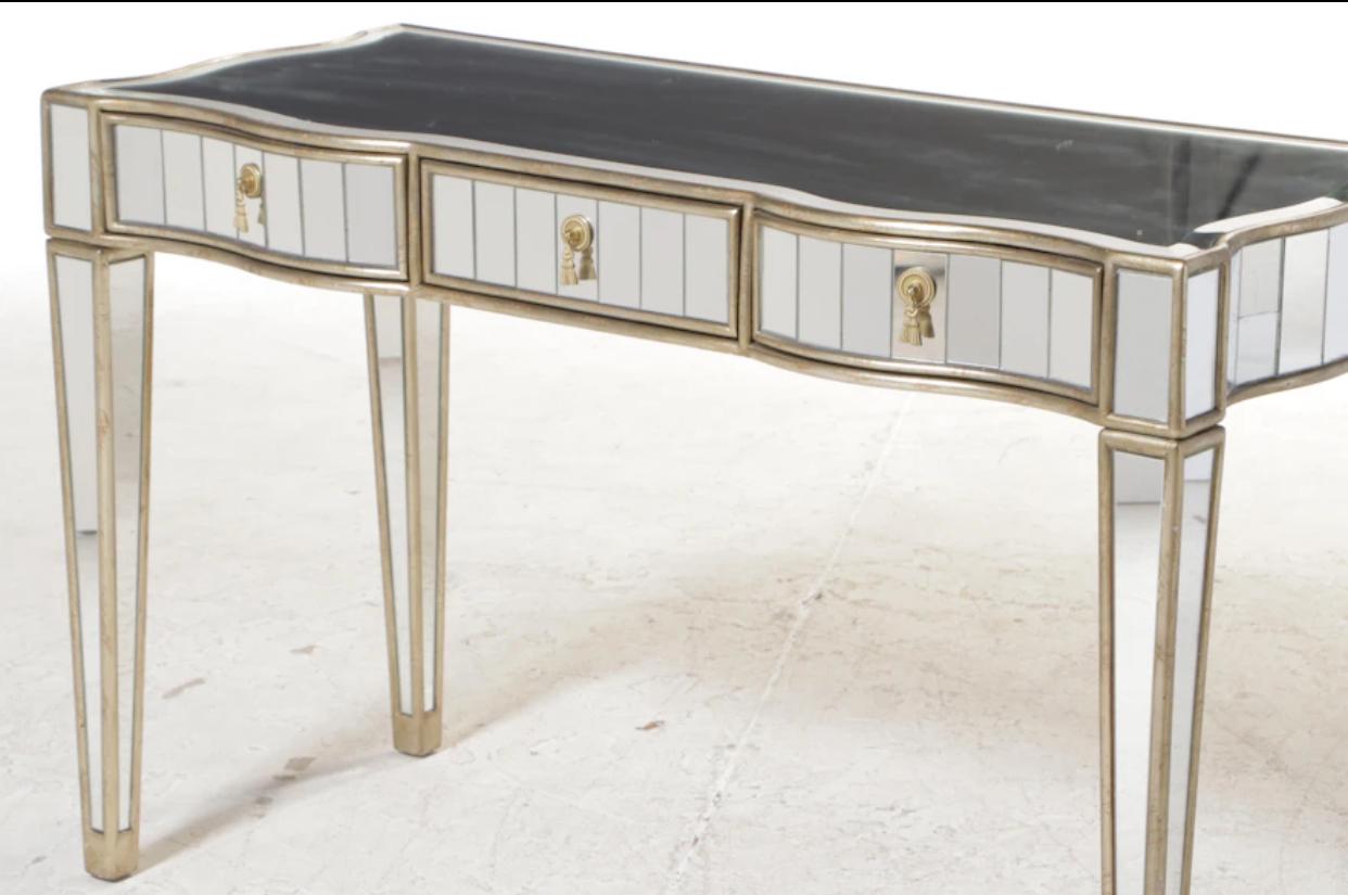 Klassischer Hollywood Regency Art Deco Konsolentisch mit Spiegeln von Drexel Heritage. Verspiegelte Paneele an der Vorderseite und an den Seiten mit spitz zulaufenden und verspiegelten Beinen. Abgeschrägte Spiegelplatte mit gerundeten Kanten.