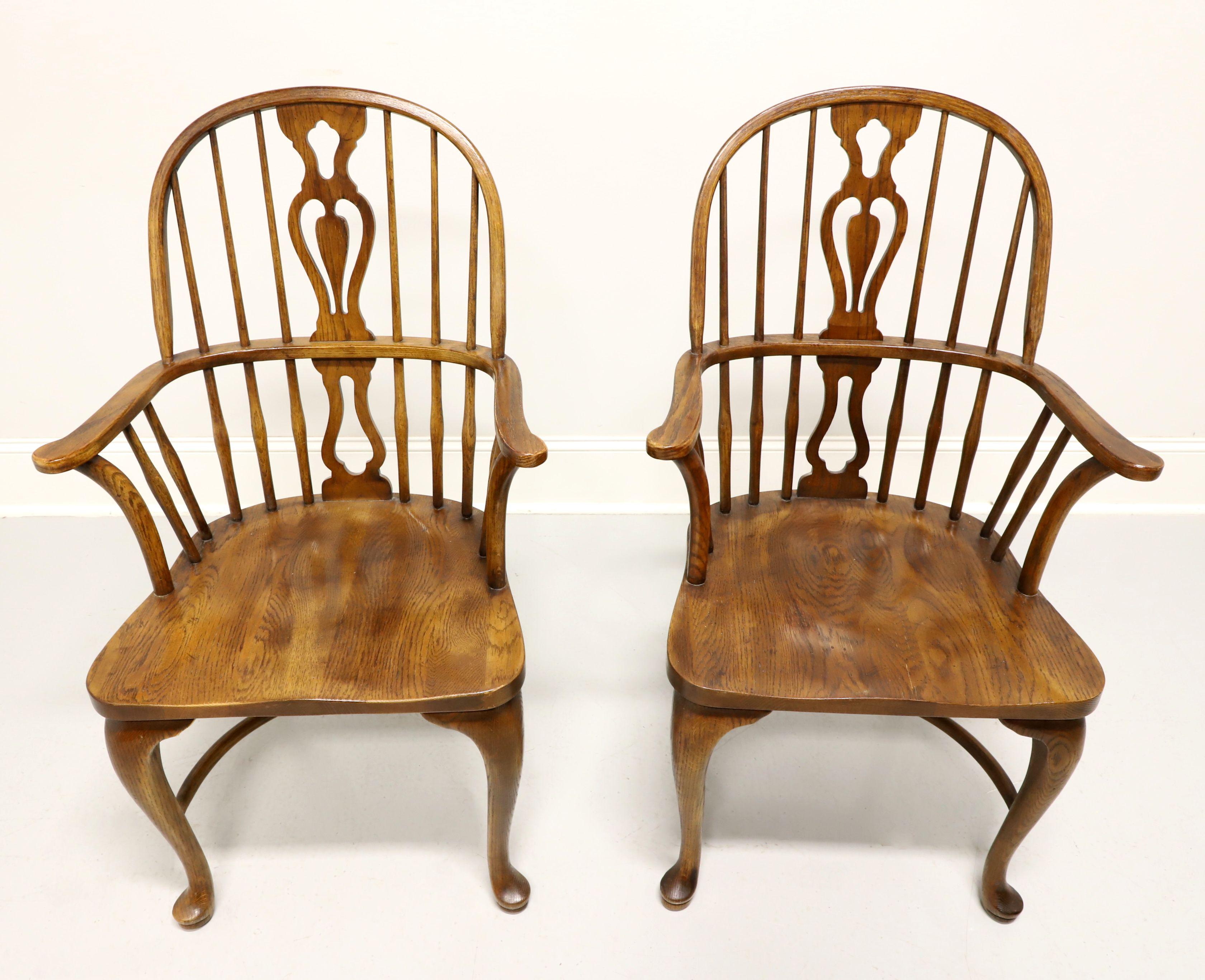 A pair of Windsor style dining armchairs by Drexel Heritage. Solid oak, hoop back with spindles, decoratively carved backrest, cross the back curved arms with support spindles, saddle shape seat, cabriole front legs with pad feet, turned back legs