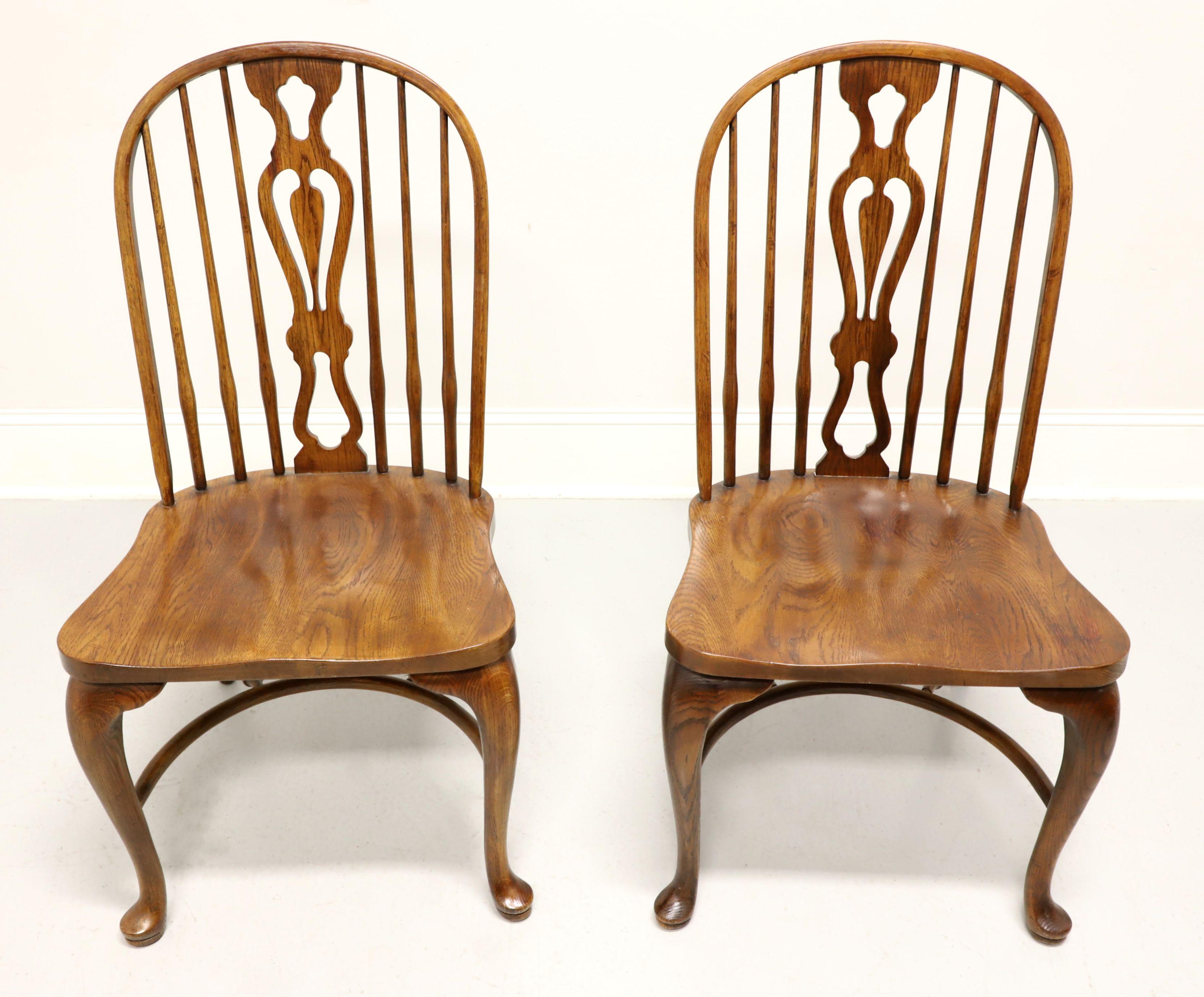 A pair of Windsor style dining side chairs by Drexel Heritage. Solid oak, hoop back with spindles, decoratively carved backrest, saddle shape seat, cabriole front legs with pad feet, turned back legs and arched front stretcher with turned back
