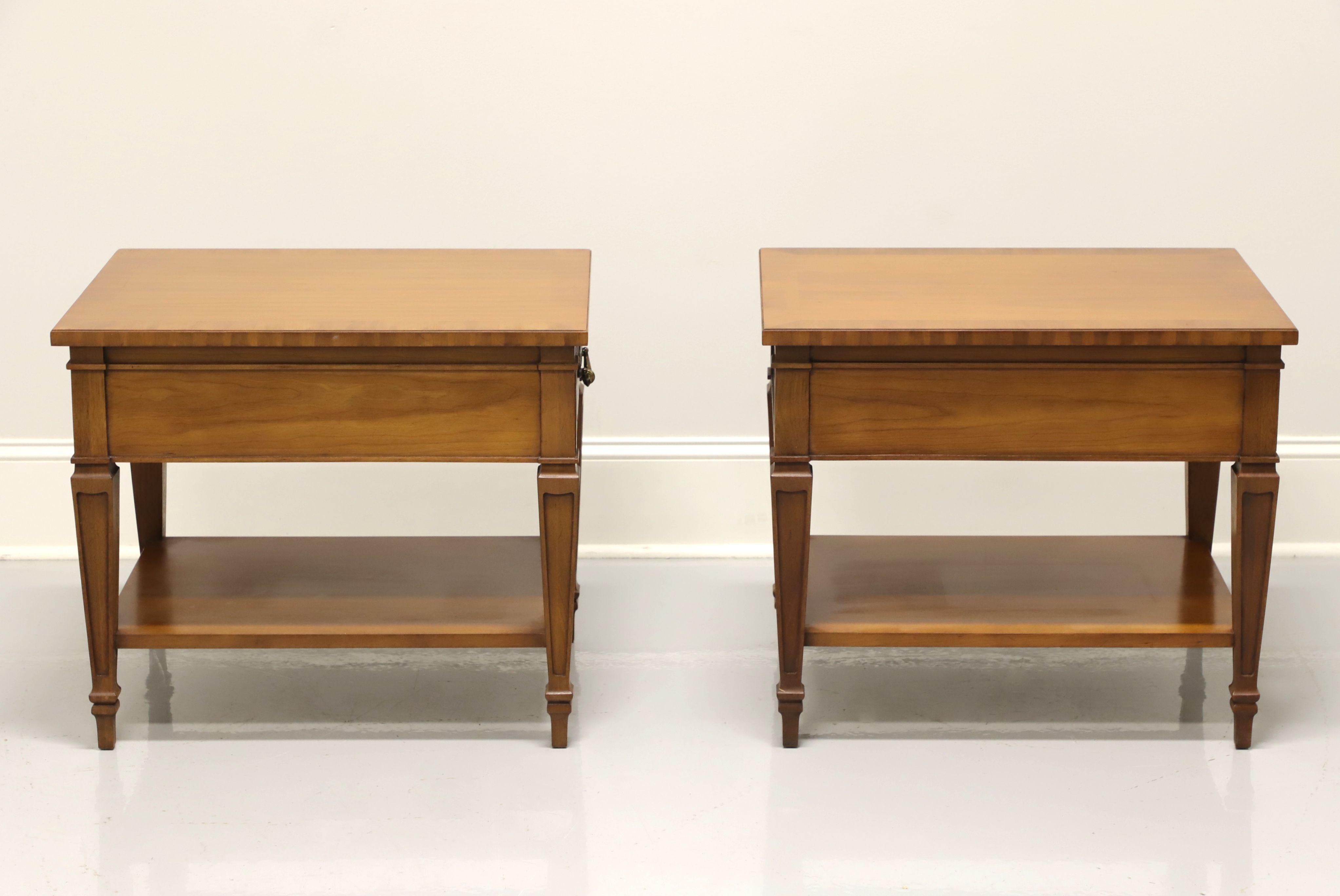 A pair of mid-century side tables by Drexel Heritage, from their Repertoire Collection. Walnut with banded top, brass hardware, undertier shelf and spade feet. Features burl to drawfront of one drawer of dovetail construction. Made in North