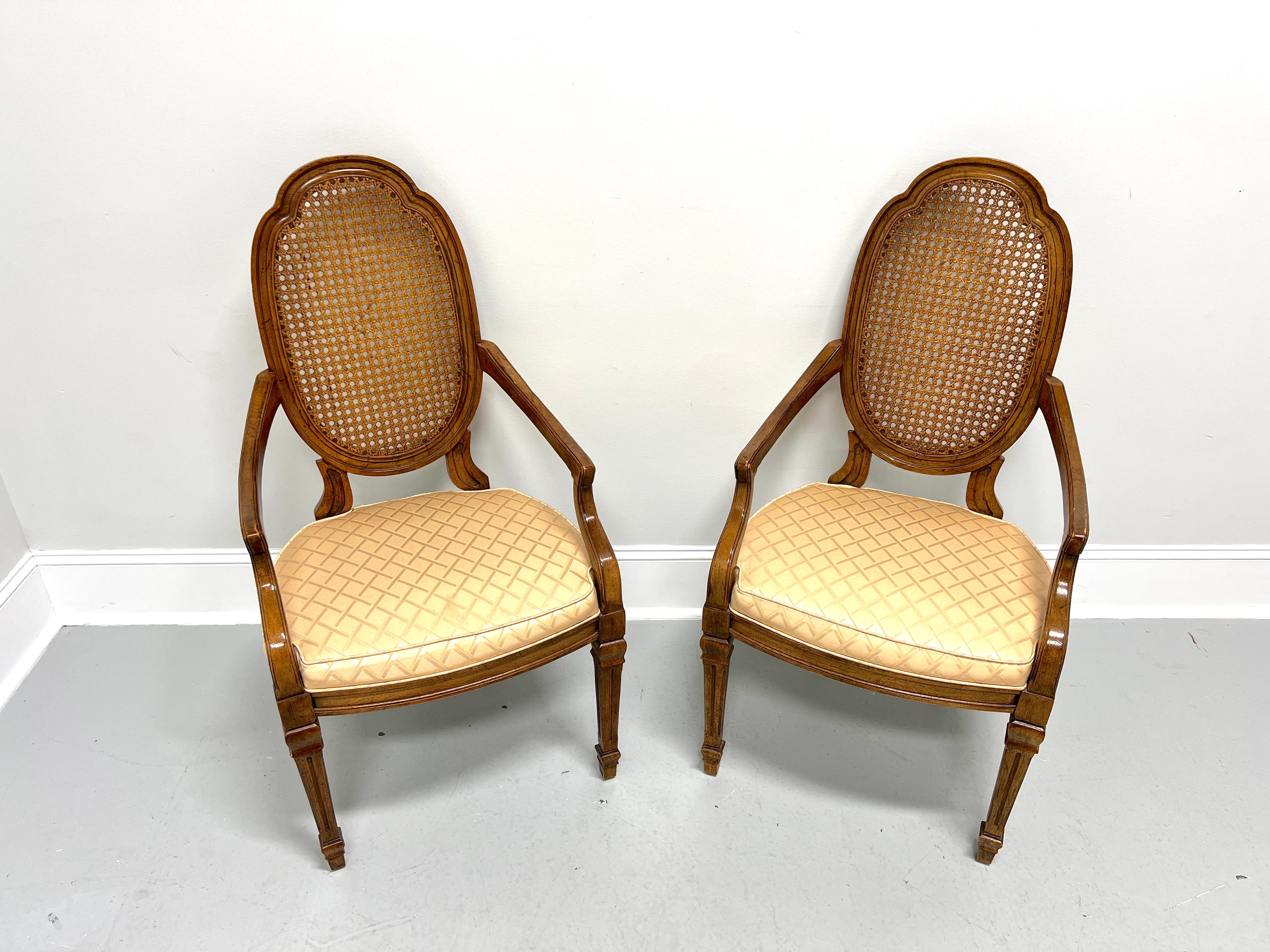 A pair of French Provincial Louis XVI style dining armchairs by Drexel Heritage. Walnut with a slightly distressed finish, carved oval shield-like caned backs, sloping straight arms with curved supports, gold color diamond pattern fabric upholstered
