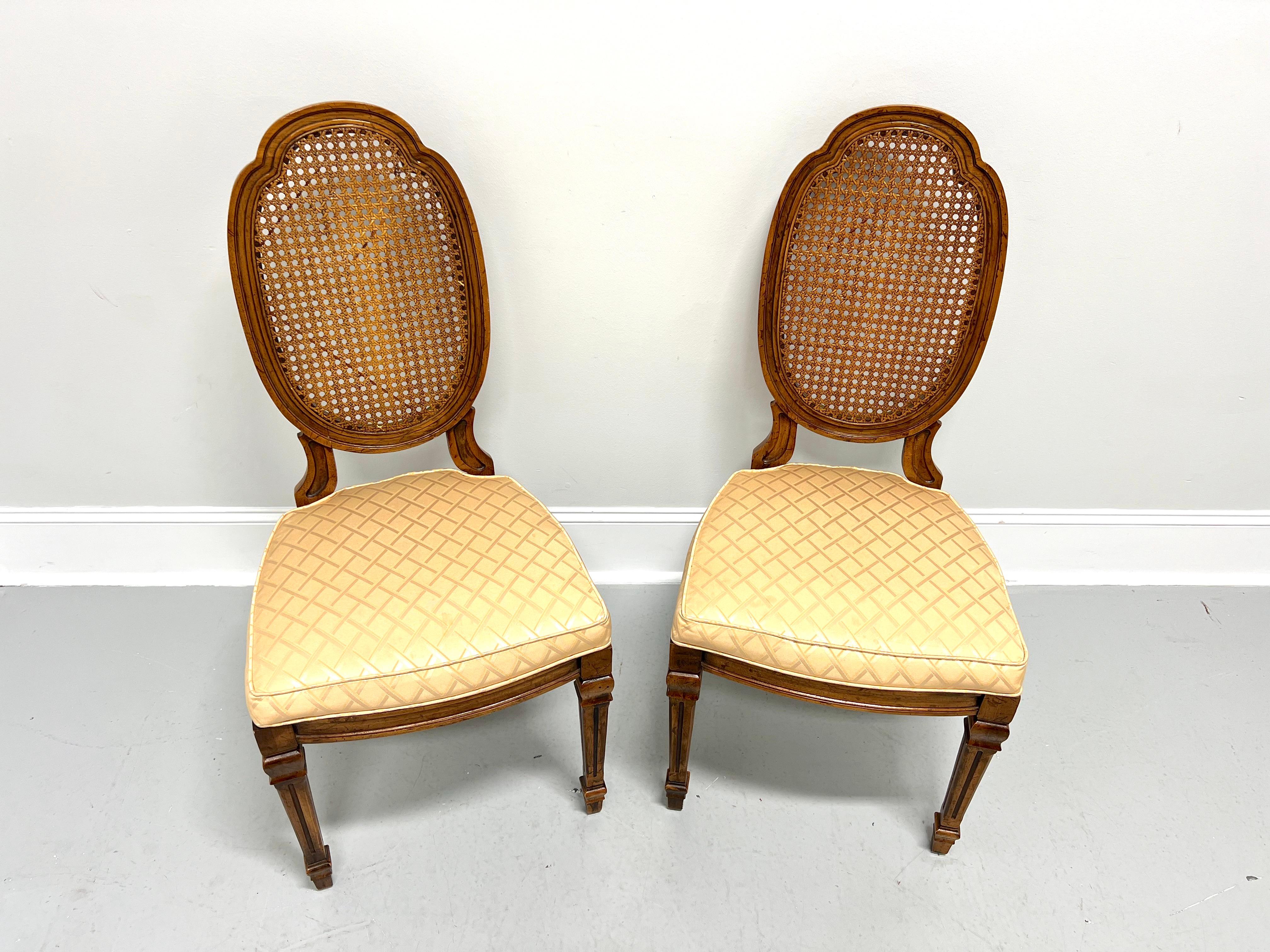 A pair of French Provincial Louis XVI style dining side chairs by Drexel Heritage. Walnut with a slightly distressed finish, carved oval shield-like caned backs, gold color diamond pattern fabric upholstered seats, carved apron, tapered fluted