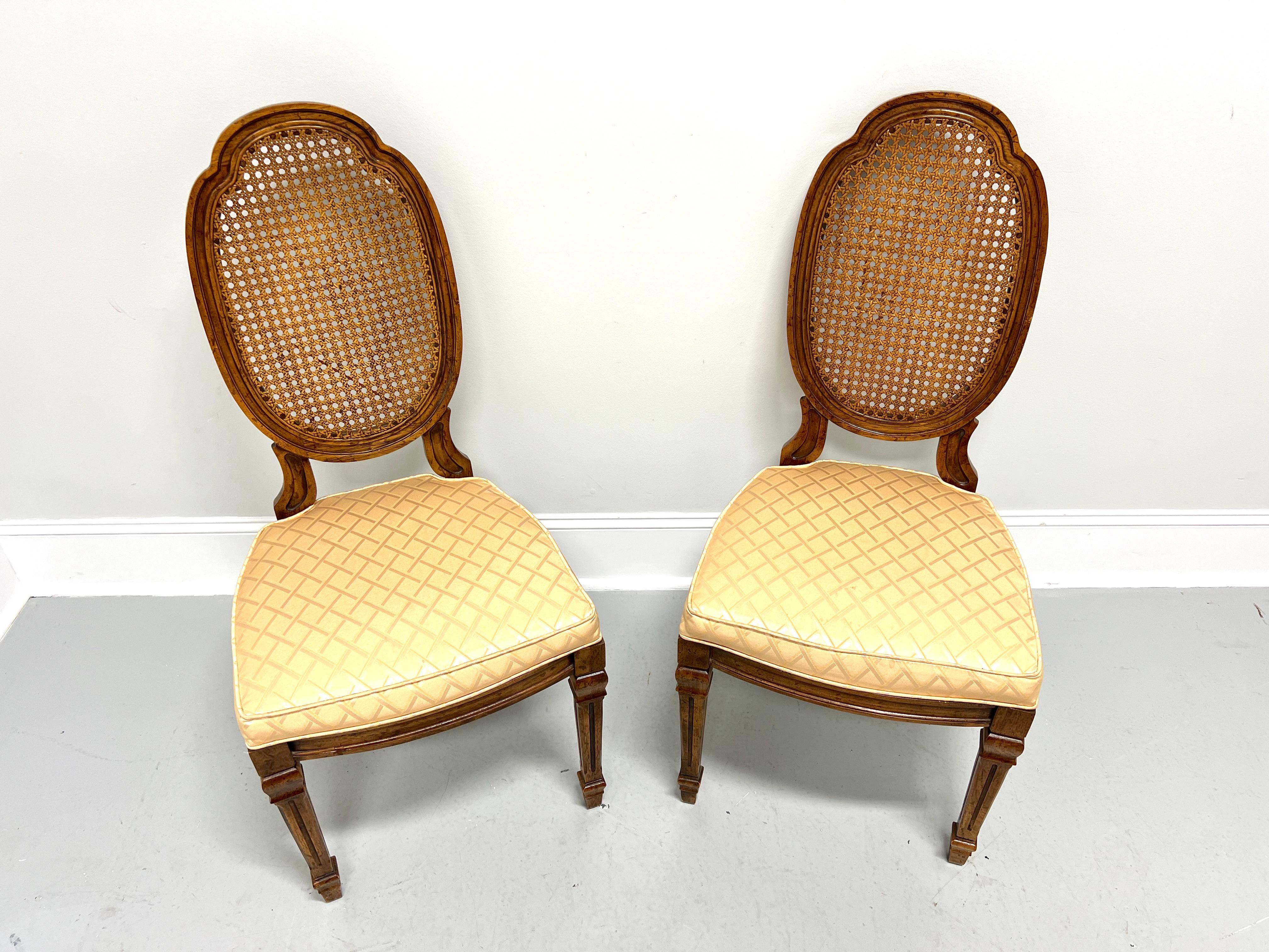 A pair of French Provincial Louis XVI style dining side chairs by Drexel Heritage. Walnut with a slightly distressed finish, carved oval shield-like caned backs, gold color diamond pattern fabric upholstered seats, carved apron, tapered fluted