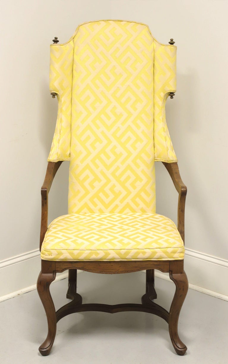 A Spanish style wing back chair by Drexel. Walnut frame with a distressed finish, very high slender back, brass finials to wings lend a scroll appearance, cabriole front legs and stretcher base. Features a yellow and white color patterned fabric