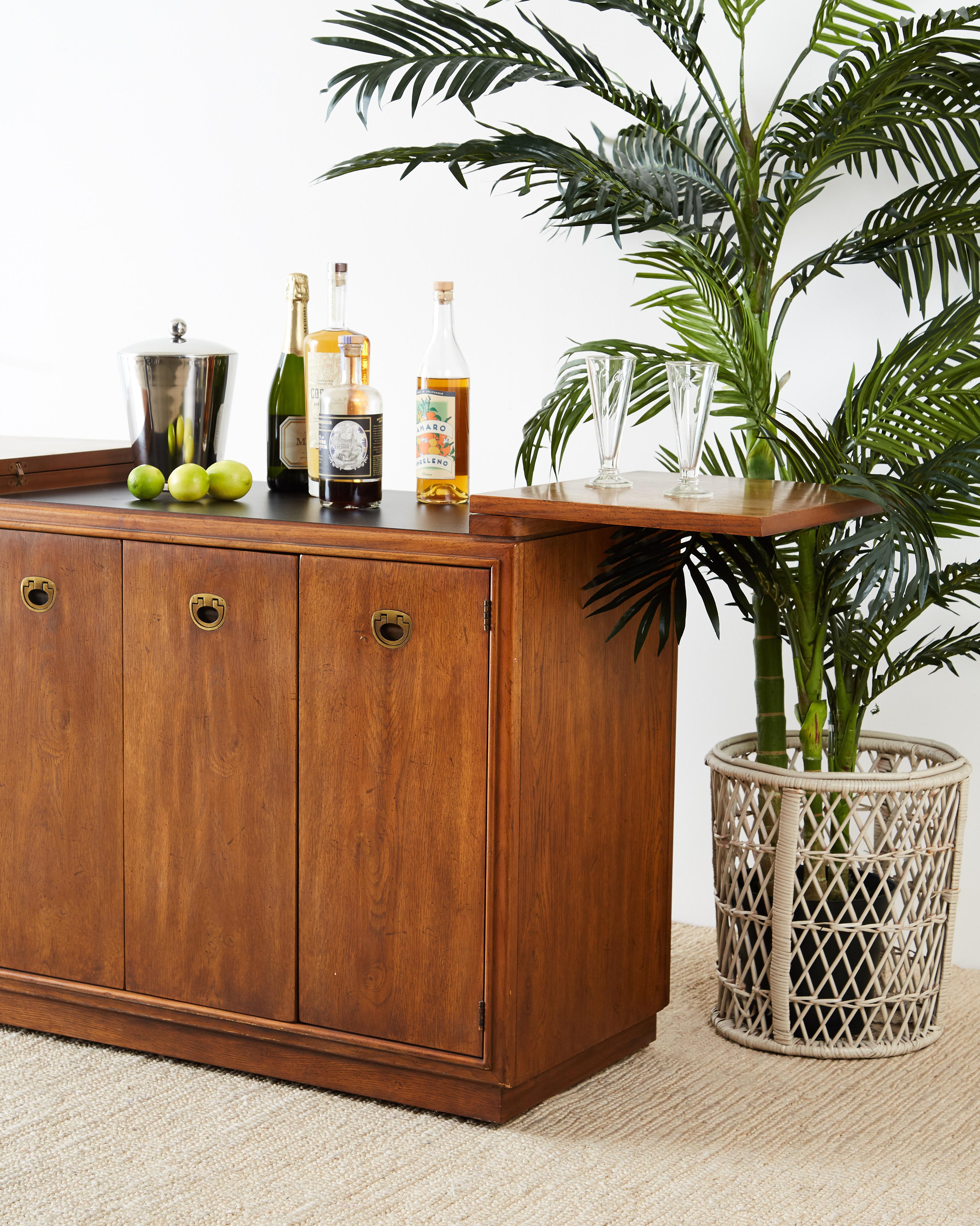 Fabulous midcentury rolling bar cart, dry bar or server by Drexel. Constructed from beautifully grained walnut and finished on all sides. Made in the Campaign style with a flip topextending top which reveals a formica black work surface. Three doors