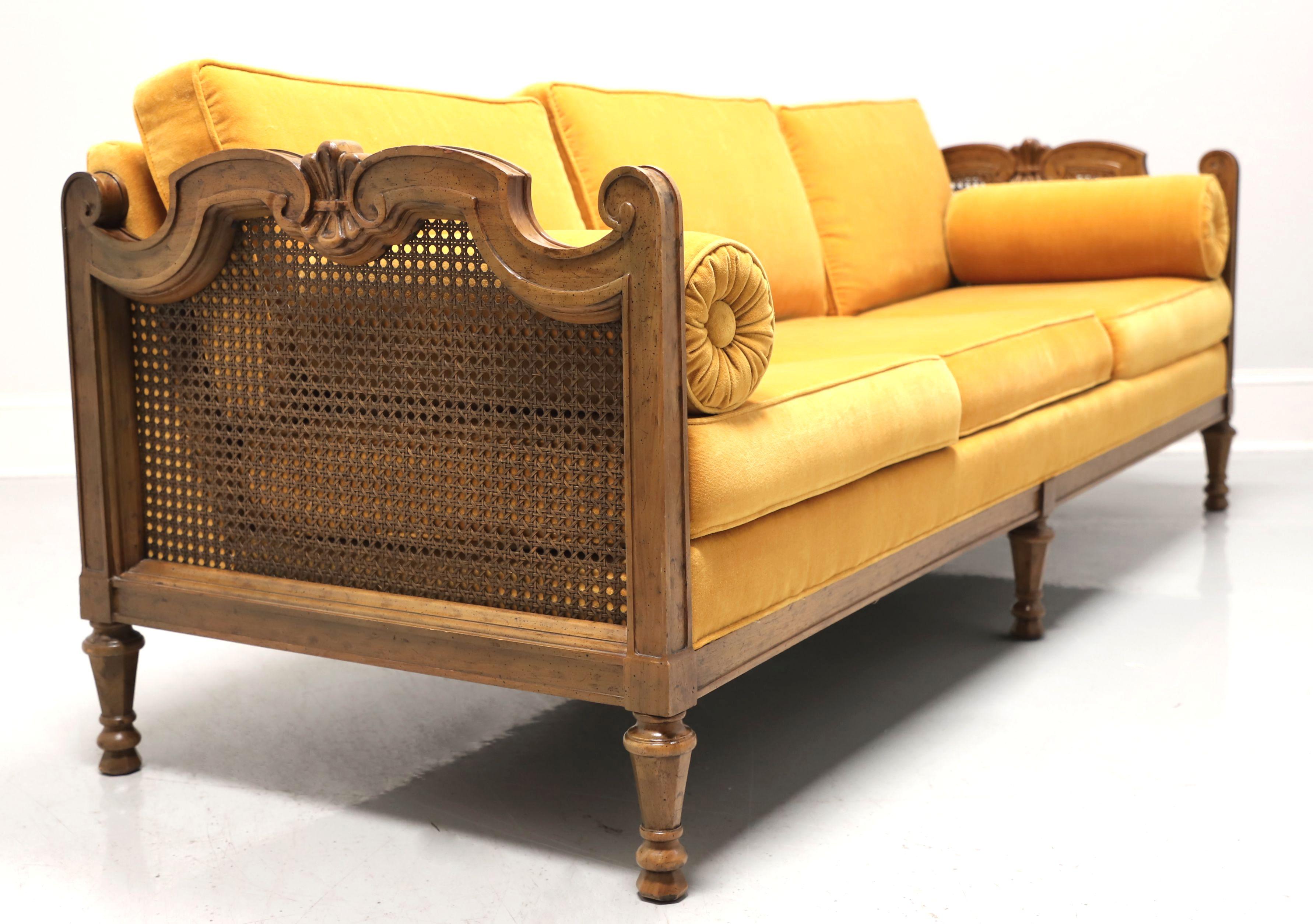 A Spanish style sofa by Drexel, from their Velero Collection. Pecan with a distressed finish, cane to sides of decoratively carved arms and six turned tapered legs. Gold color velvet fabric upholstered back, seat & back cushions and armrest