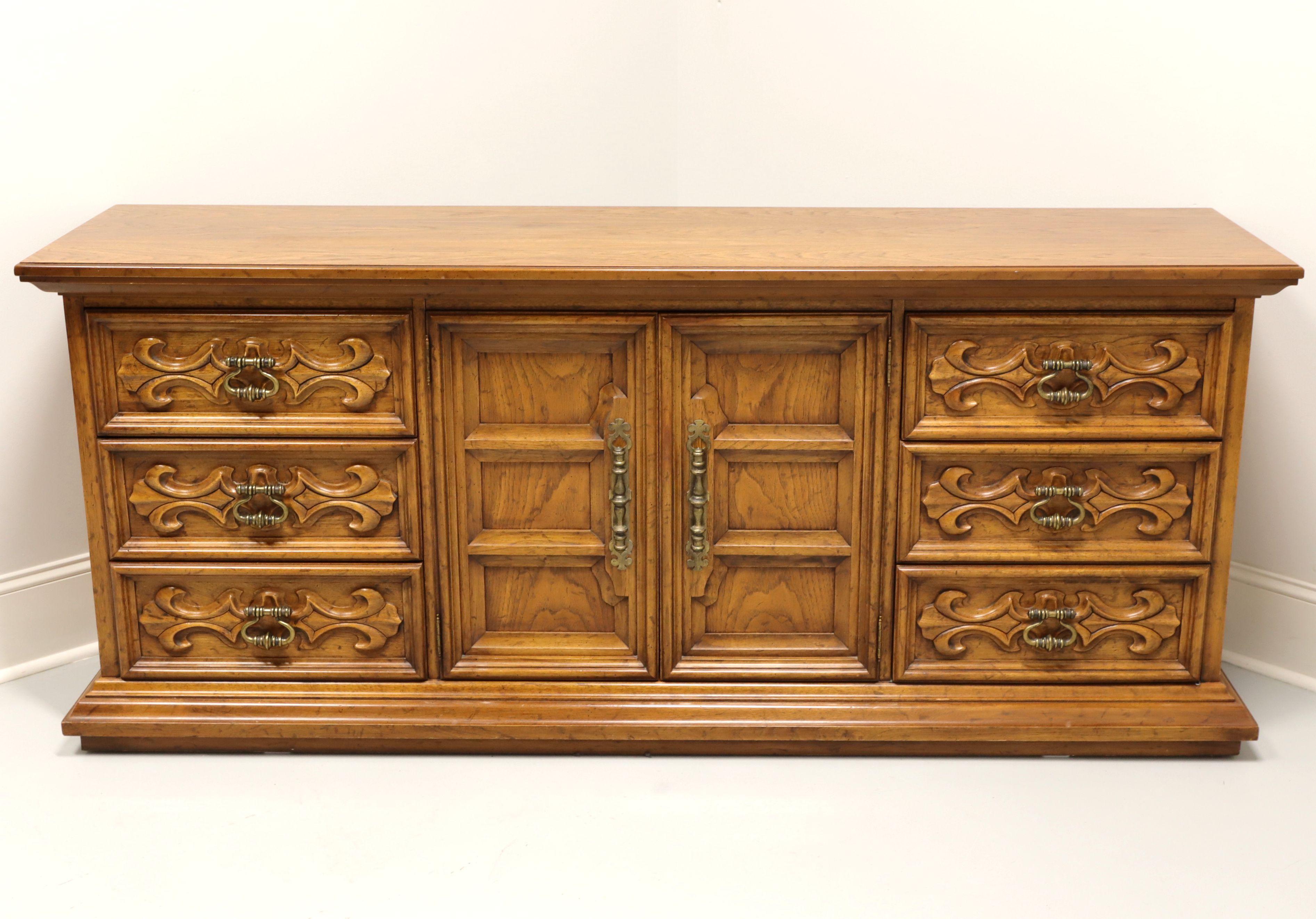 A Spanish style triple dresser by Drexel, from their Velero Collection. Pecan with a distressed finish, brass hardware, carved door and drawer fronts. Features nine drawers of dovetail construction, with three center drawers being behind solid dual