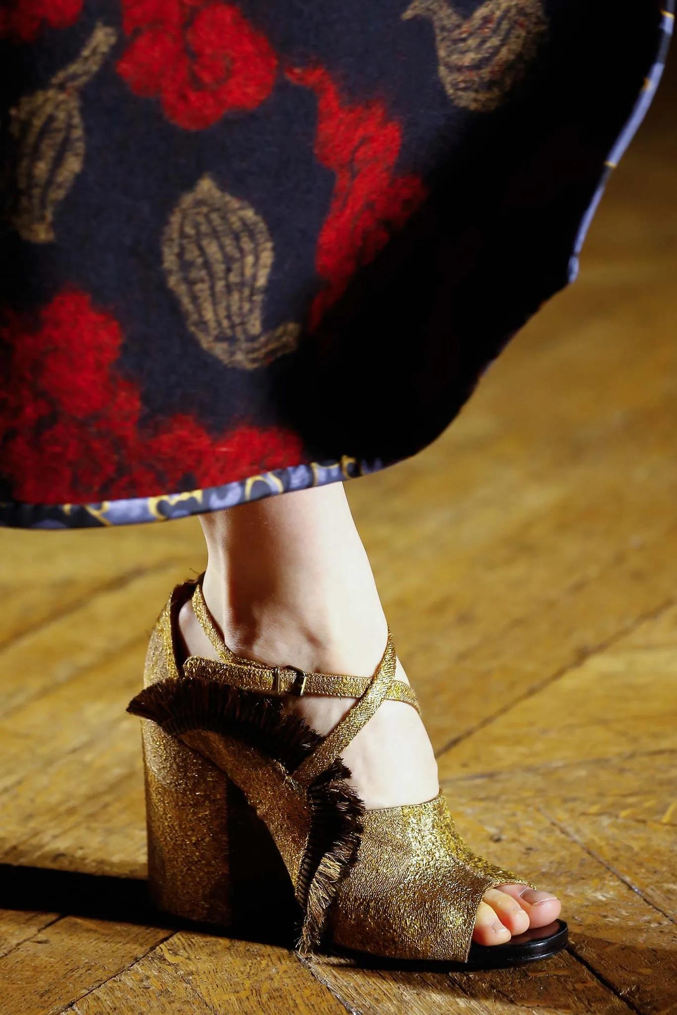 Sandales à talon bloc en brocart doré avec bride cheville de Dries Van Noten, issues de la collection du défilé automne-hiver 2015.

Il est doté d'orteils ouverts arrondis et d'une bride de cheville croisée sur le devant. Franges rayées noires et