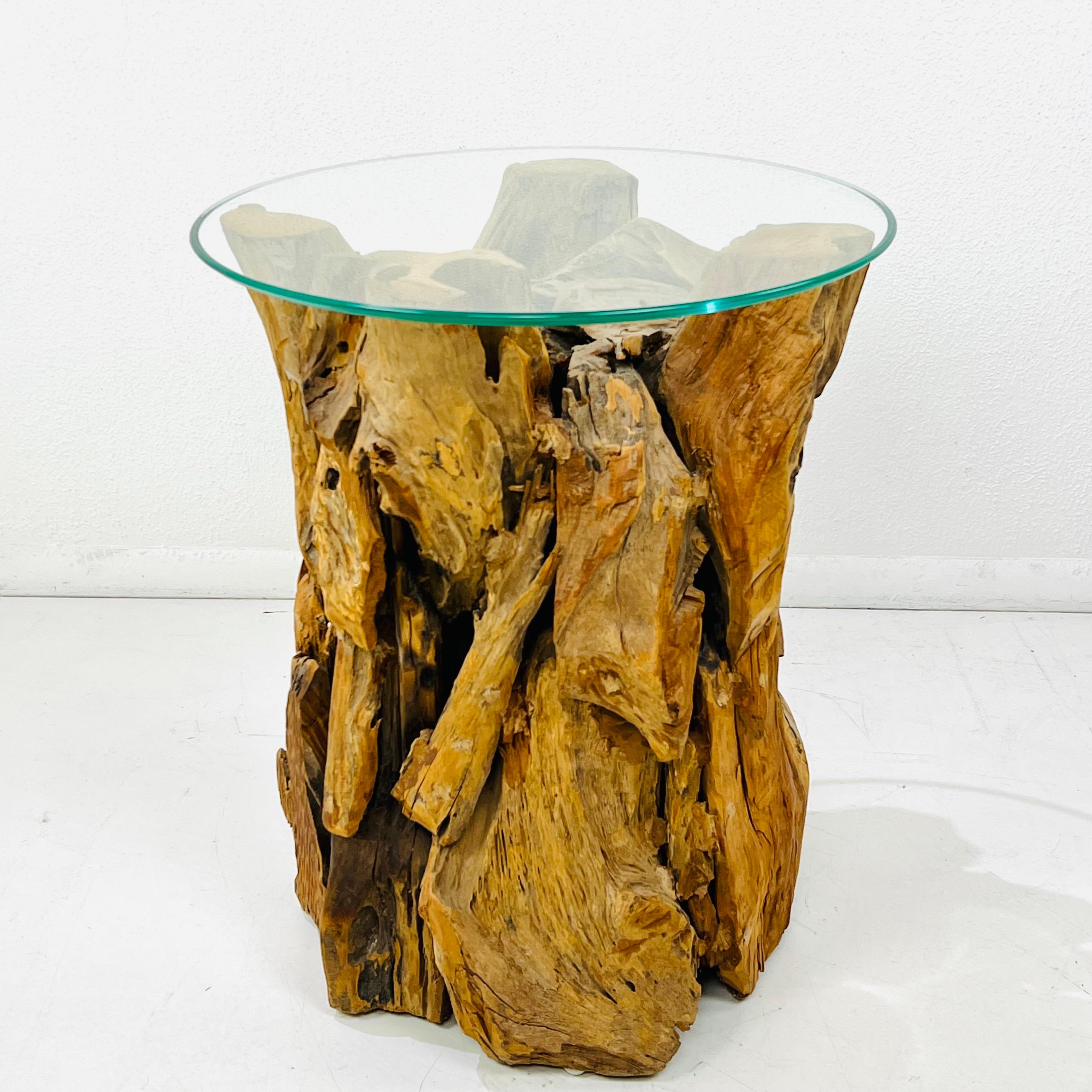 Cette table sculpturale est fabriquée à partir d'un groupe de bois flotté dense et magnifiquement altéré par les intempéries. Un épais plateau circulaire en verre flotte au-dessus du bois, ajoutant un contraste net et moderne qui met en valeur la