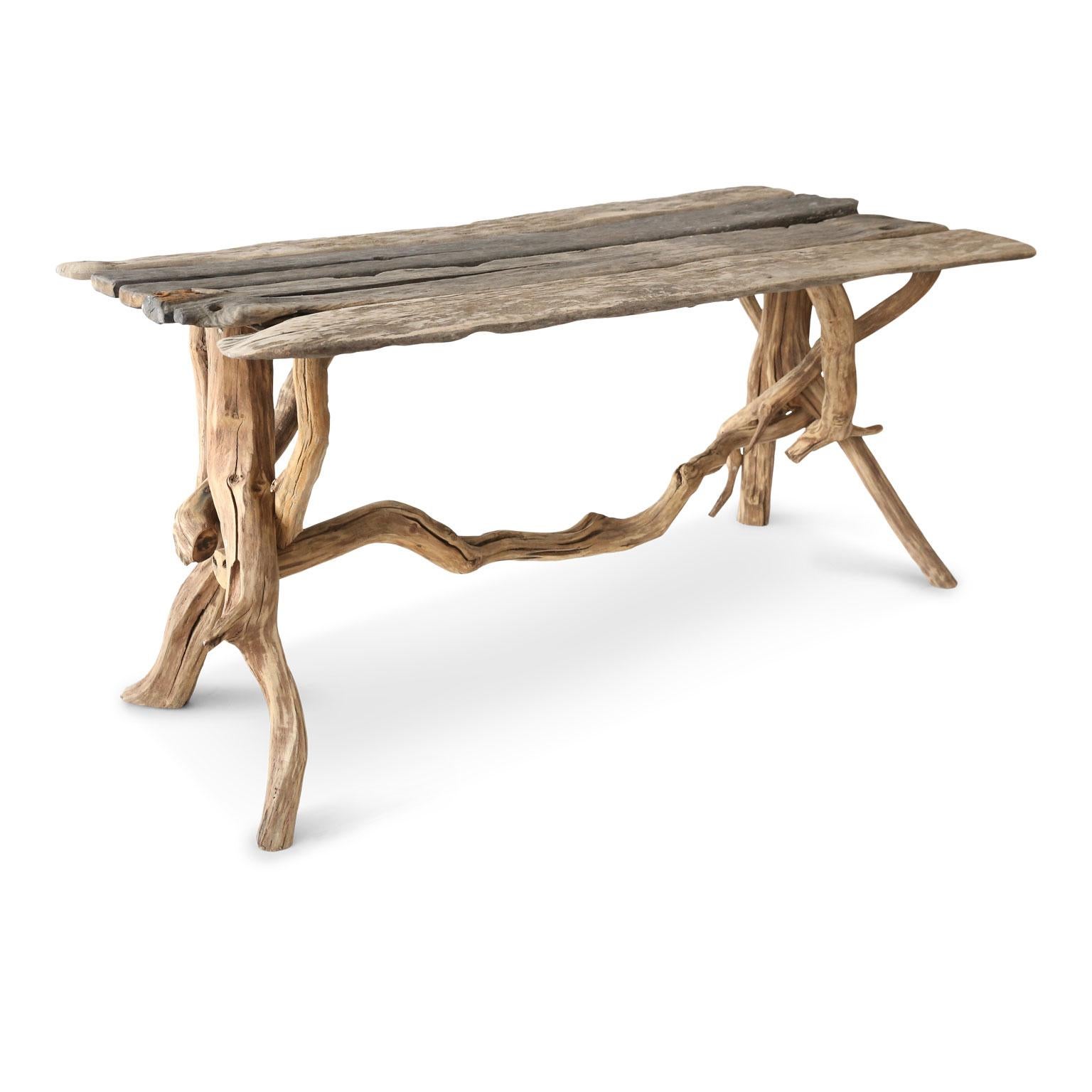 Driftwood table constructed with a graceful, natural-shaped trestle base supporting a rectangular top of naturally weathered antique planks.