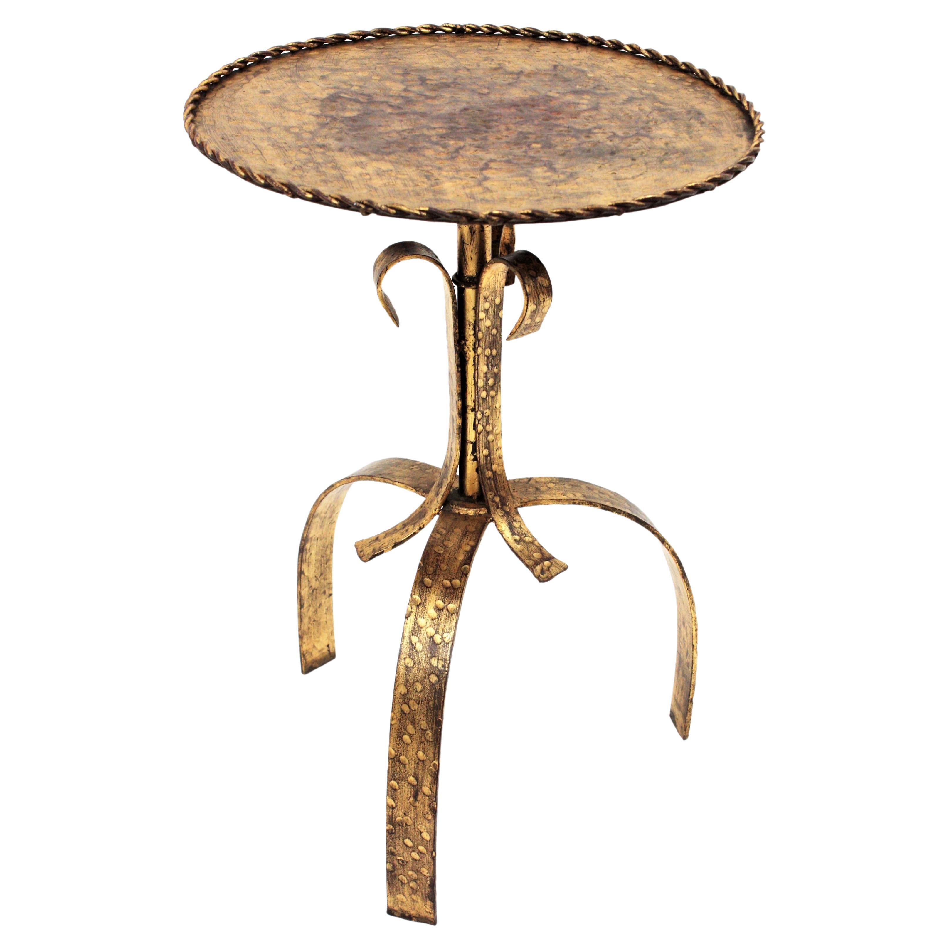 Gilt wrought iron gueridon end drinks table standing on a tripod base, Spain, 1940s.
An Spanish guéridon hand-hammered table with round top and gold leaf finish. 
This side table combines Hollywood Regency and Gothic style accents. The top is