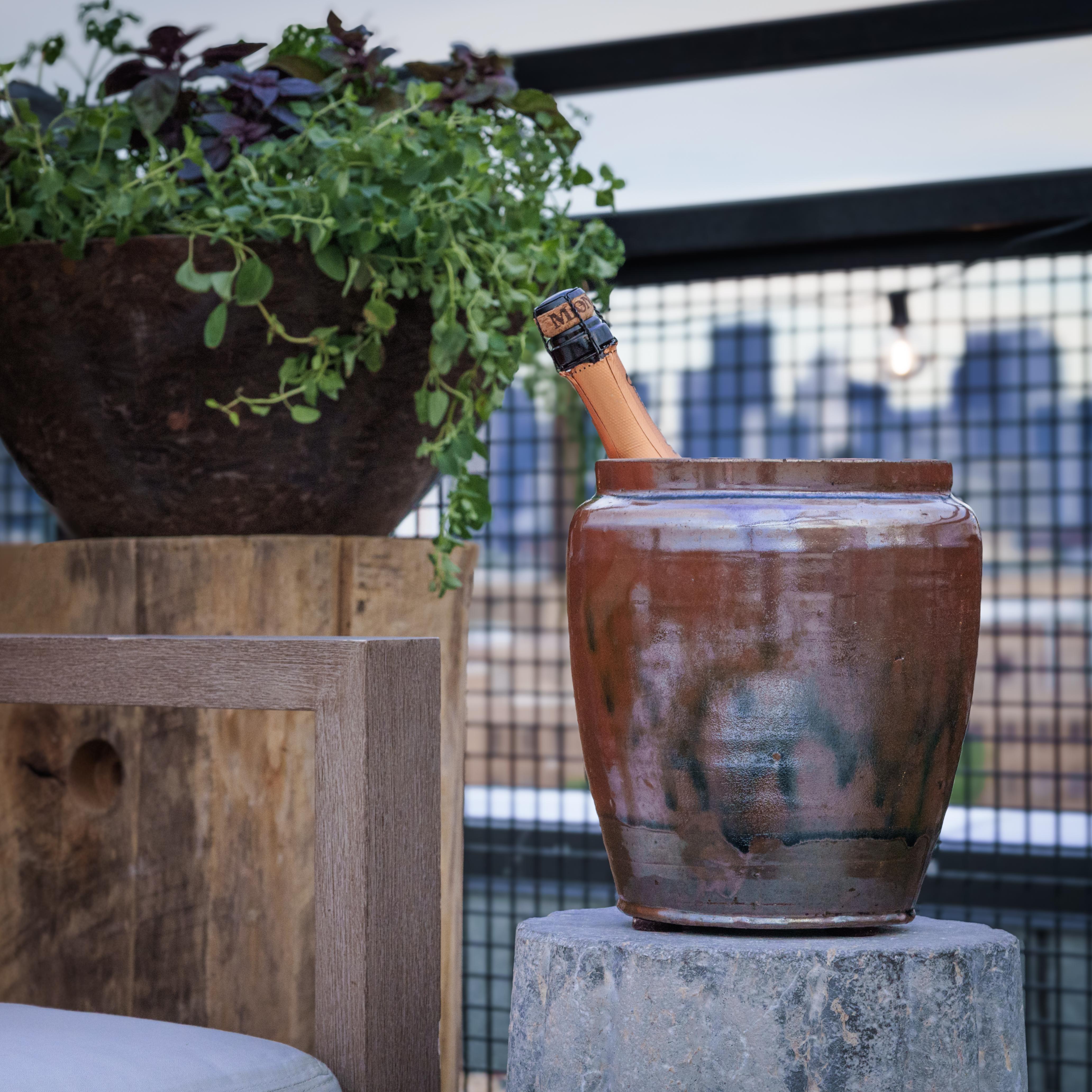 Uno smalto marrone denso e lucido ricopre la forma affusolata di questo vaso da cucina in terracotta dell'inizio del XX secolo, soffermandosi sulle imperfezioni e scintillando con una lucentezza iridescente. Come dimostra l'interno smaltato, questo