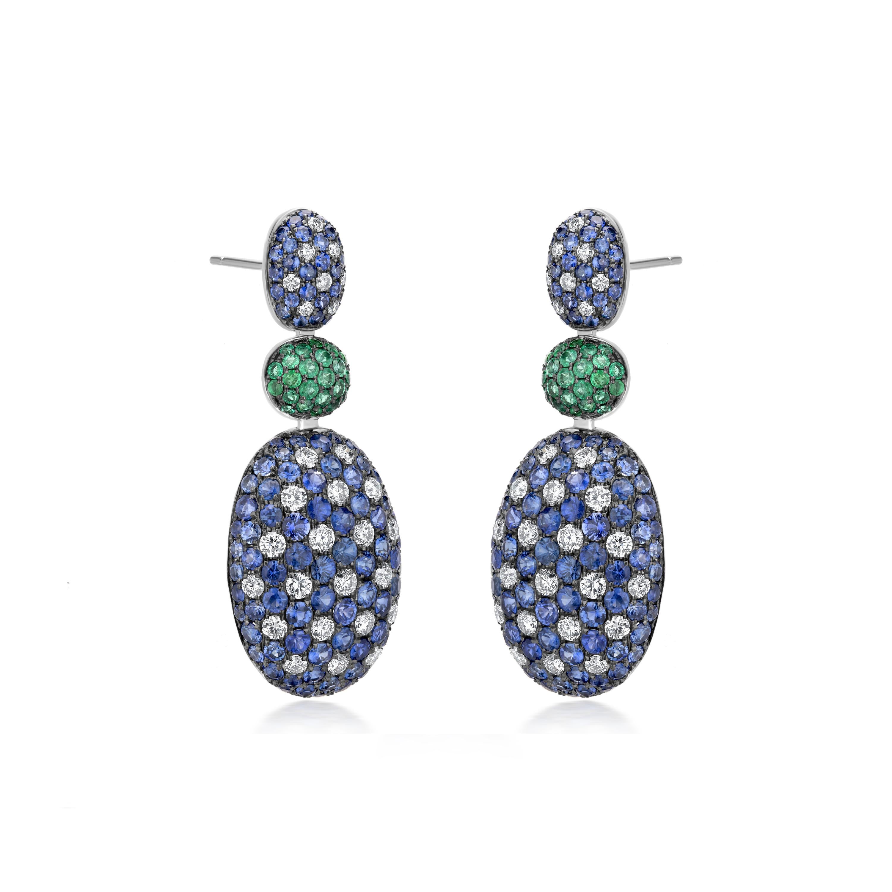 The three-tiered earring has a fantastic design by Nigaam, with an oval surmount attached to an emerald-studded circle on the second layer, and diamonds with blue sapphire on the third layer. It has a push-button closure. Its attractiveness is