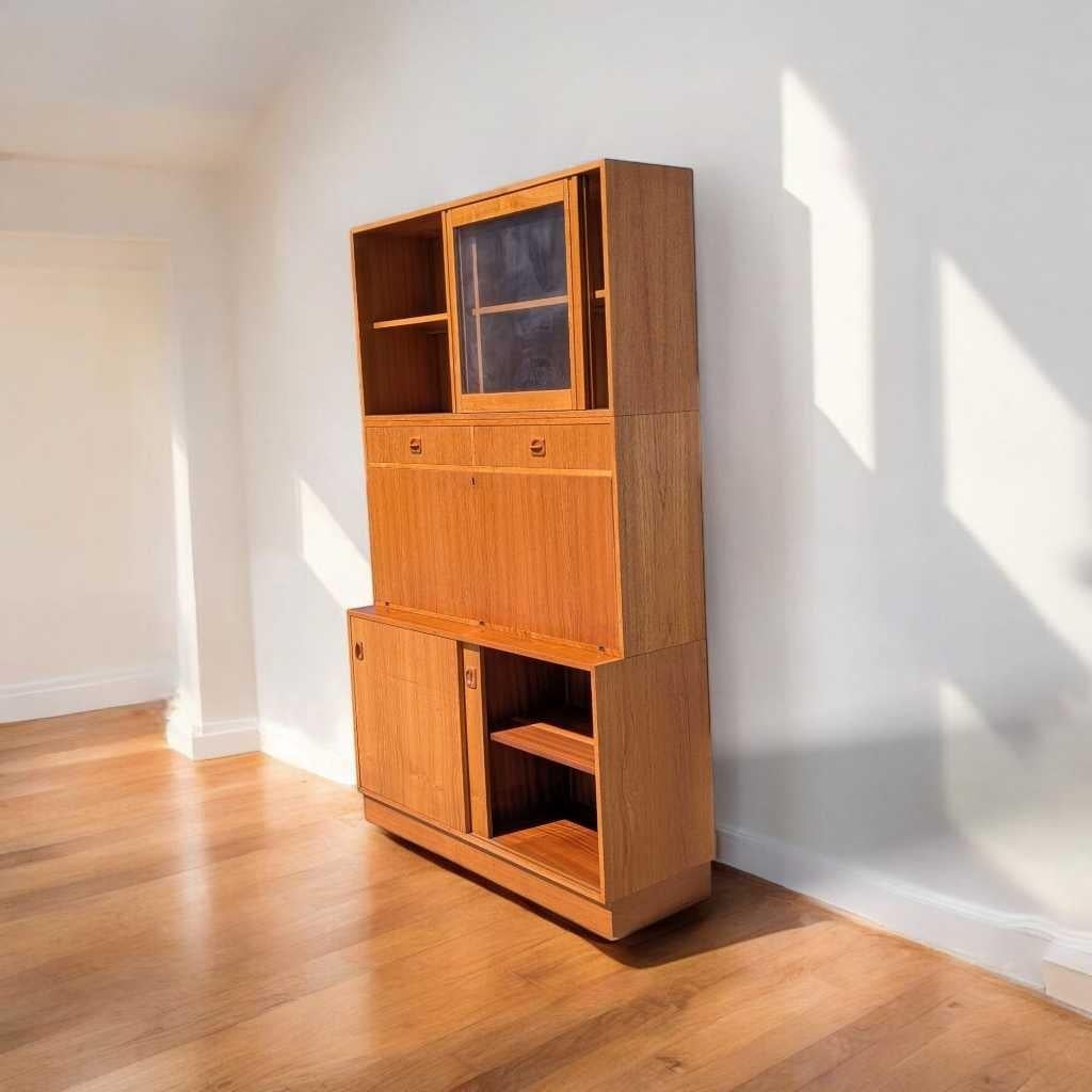 A distinctive wall unit in the mid-century modern tradition, crafted from teak veneer and showcasing clean Scandinavian lines and versatile functionality. This vintage unit features open shelving, a drop front desk that opens to a compact workspace,