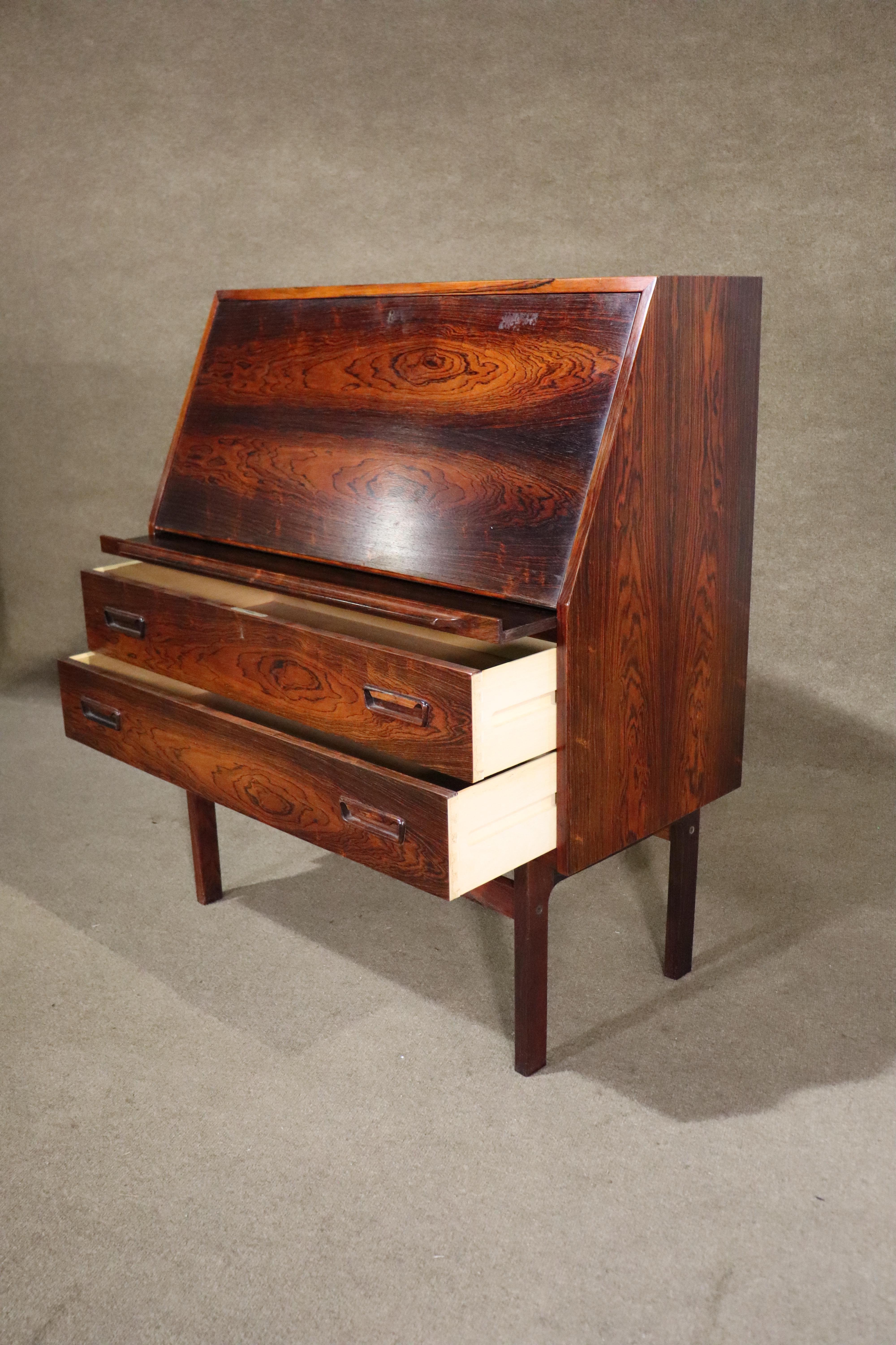 Danish made mid-century modern drop front secretary desk in rich rosewood grain. Two wide drawers for storage, drop front door becomes a writing surface, inset desk storage and drawers. A beautiful example of Danish design, complete with book