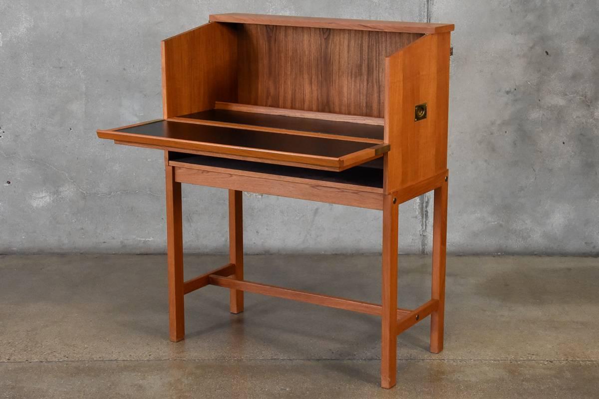 A unique drop front teak bar cabinet by Dyrlund. The top of the cabinet lifts up and pulls forward creating a large stable work surface, with recessed bottle storage in the back. This piece is finished on the rear so it can easily be used floating