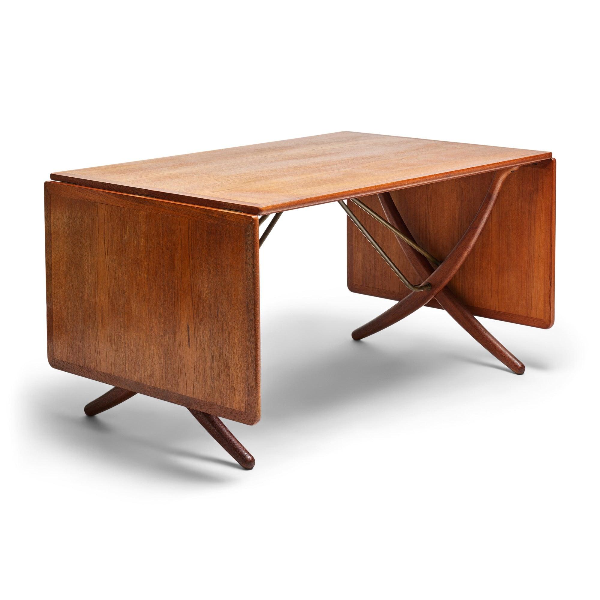 A drop-leaf dining table with a teak top, on curved, x-form oak legs with angled brass rod braces. Each leaf is 21.5