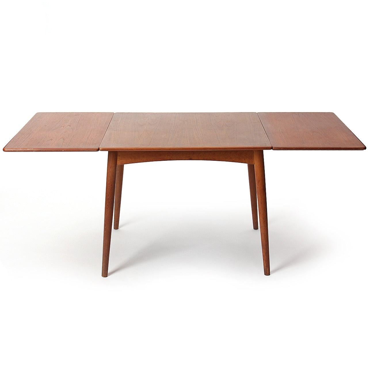 A square teak-top dining table with two drop leaves, on oak tapered dowel legs with arched aprons.