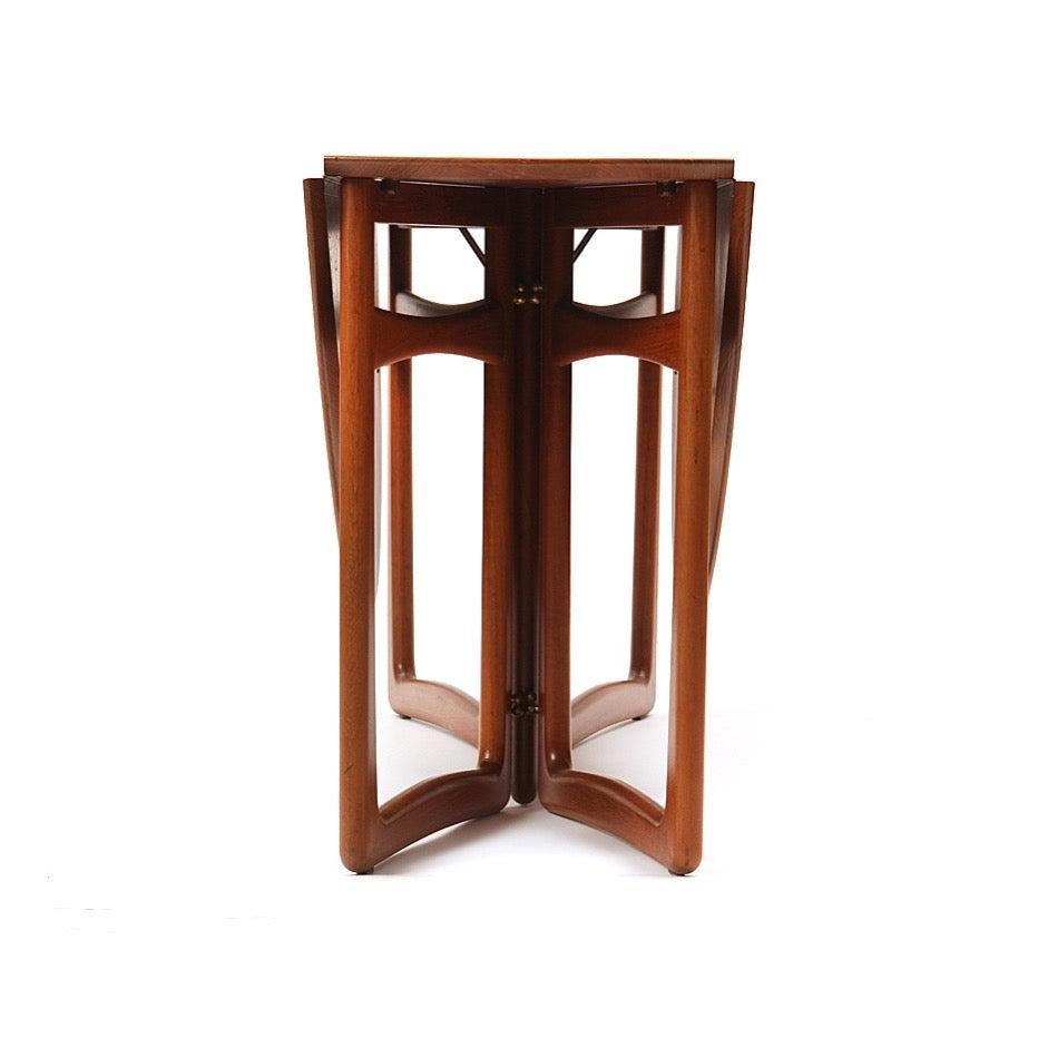 A drop leaf table in solid teak wood that can be used with one or both sides raised, sculptural legs and brass fittings. 18