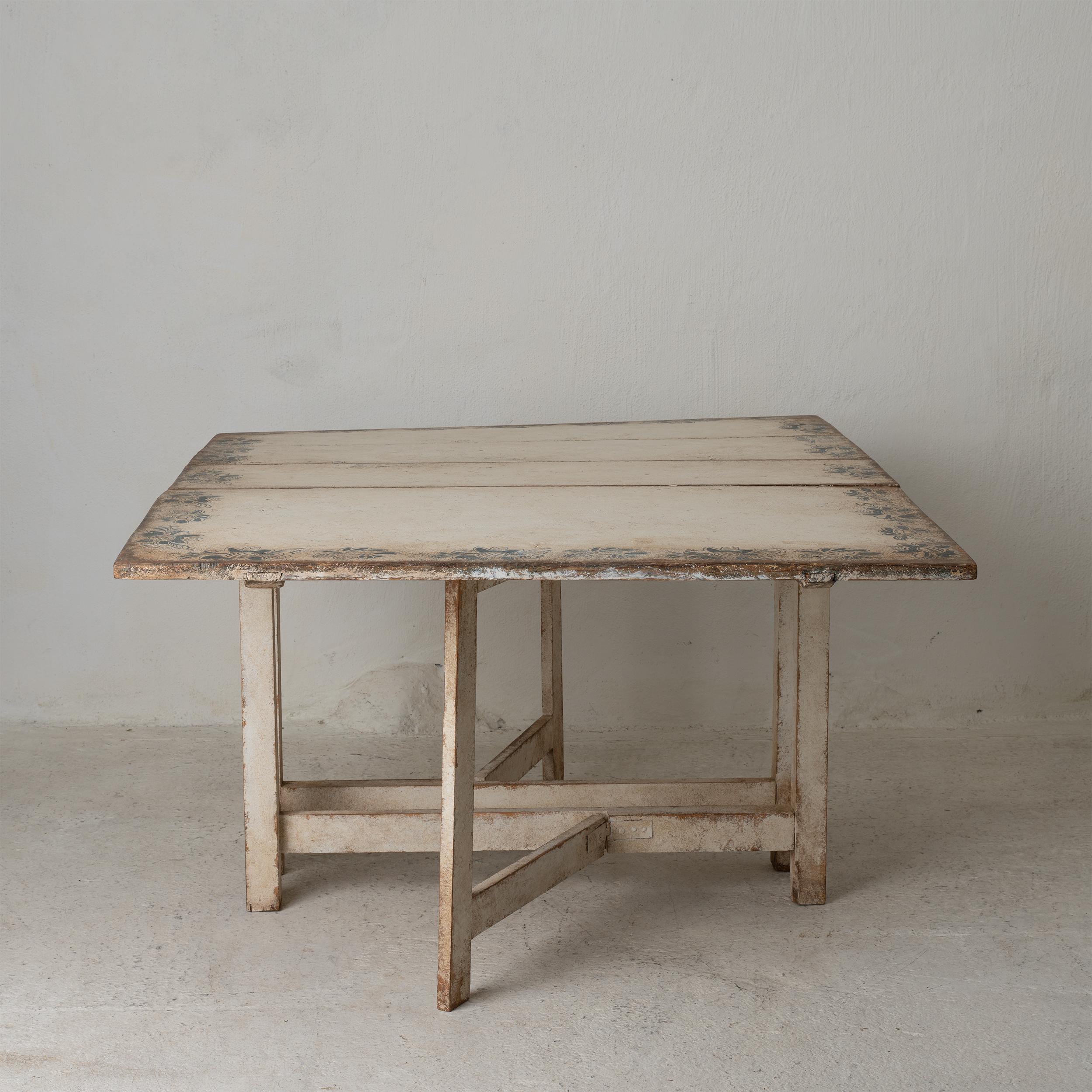 A drop-leaf table made in Sweden during the late 18th century. Later paint in a distressed white with faded blue floral bord. 